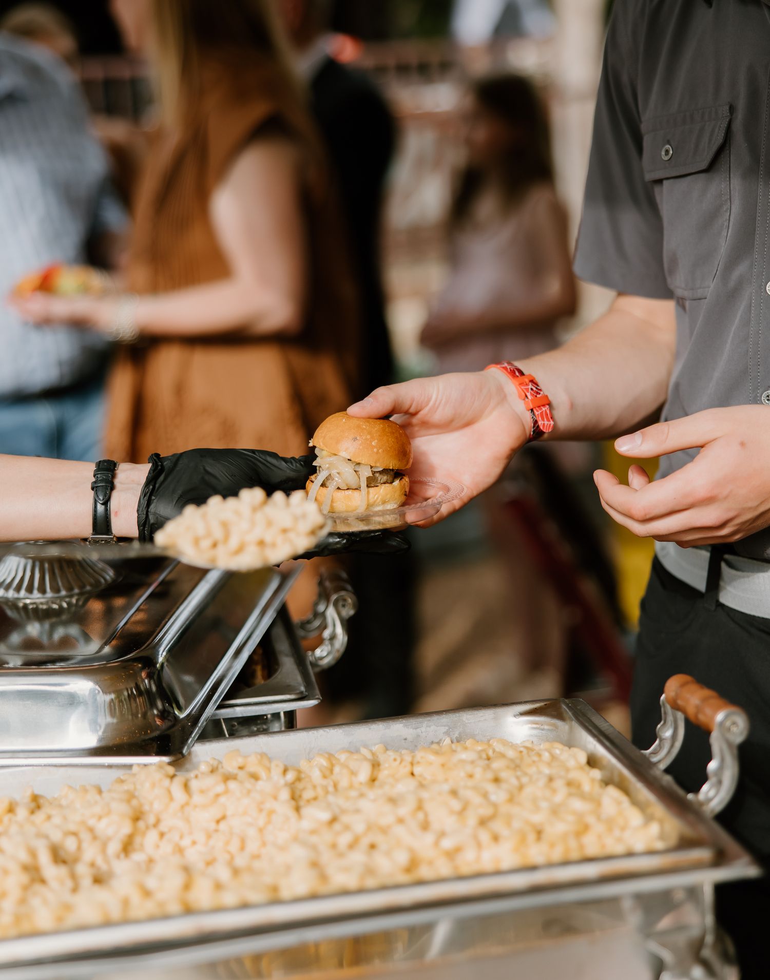 A catering staff member serves a slider burger at a wedding reception buffet with mac and cheese side dish.
