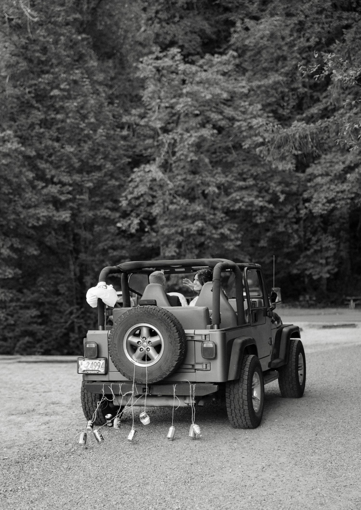 Black and white photo of a decorated Jeep Wrangler with wedding cans tied to the back bumper.