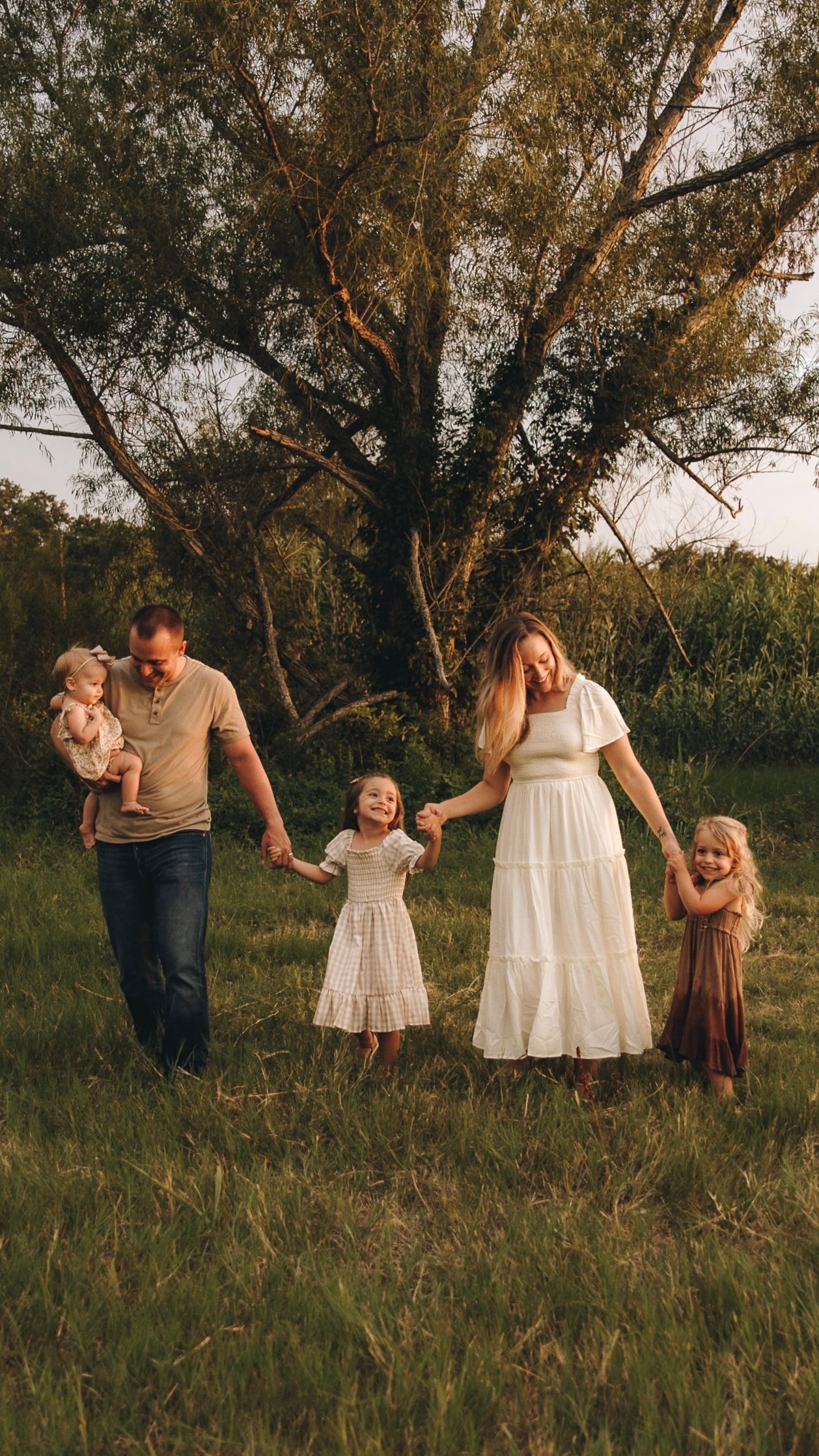 Happy family of five walking through green meadow holding hands at sunset.