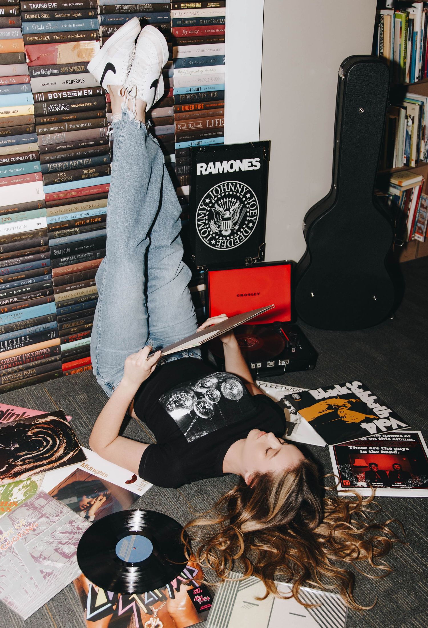Teen girl reading album cover while lying among vinyl records with Ramones poster in creative senior portrait.