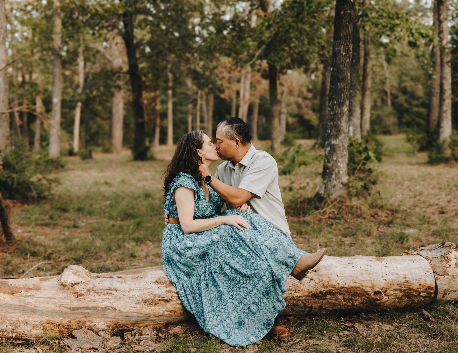 Couple sharing a kiss while sitting on a fallen log in a pine forest.