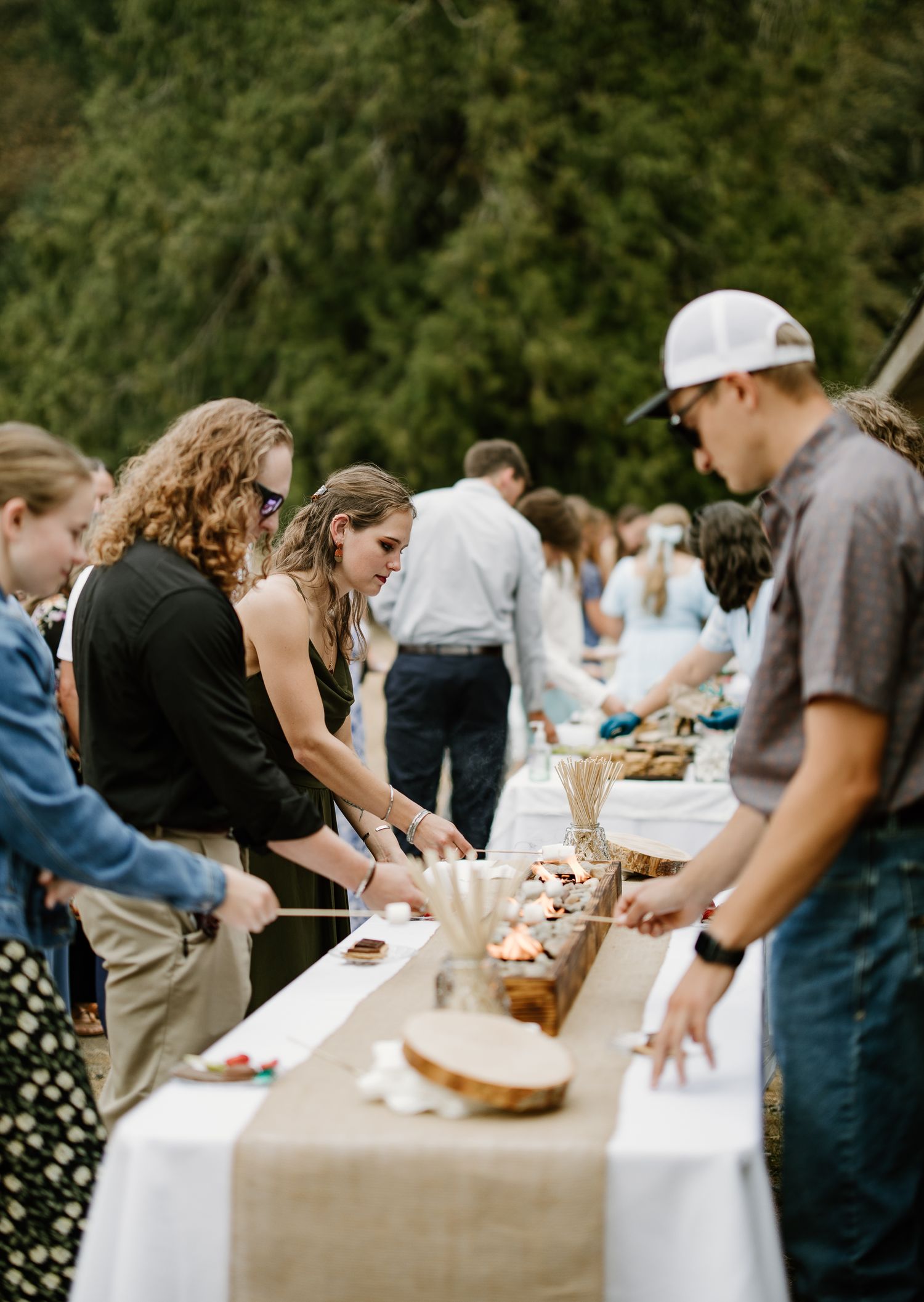 Wedding guests serve themselves at an outdoor buffet table with burlap runner at reception.