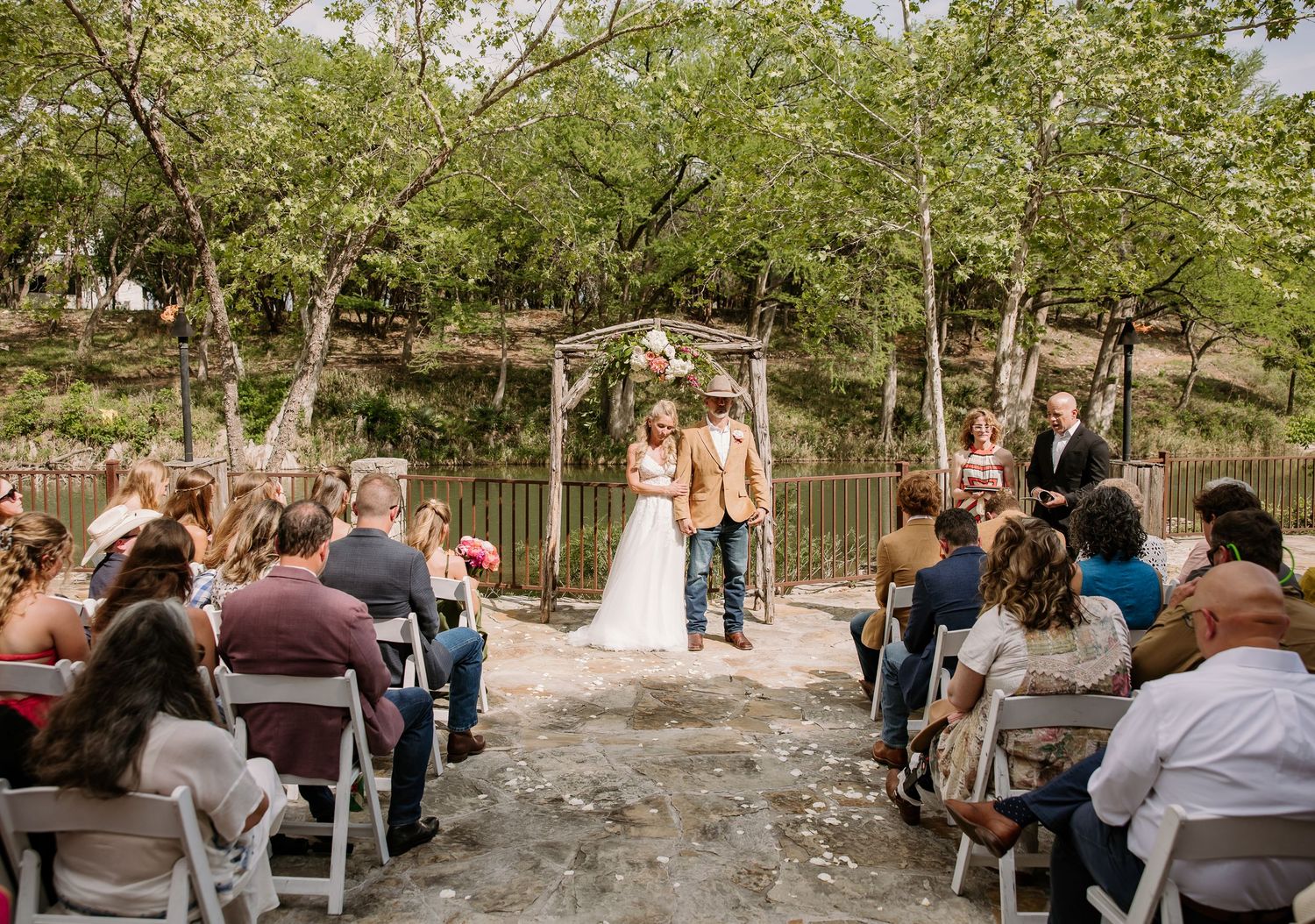 Outdoor wedding ceremony with bride and groom at altar surrounded by seated guests.