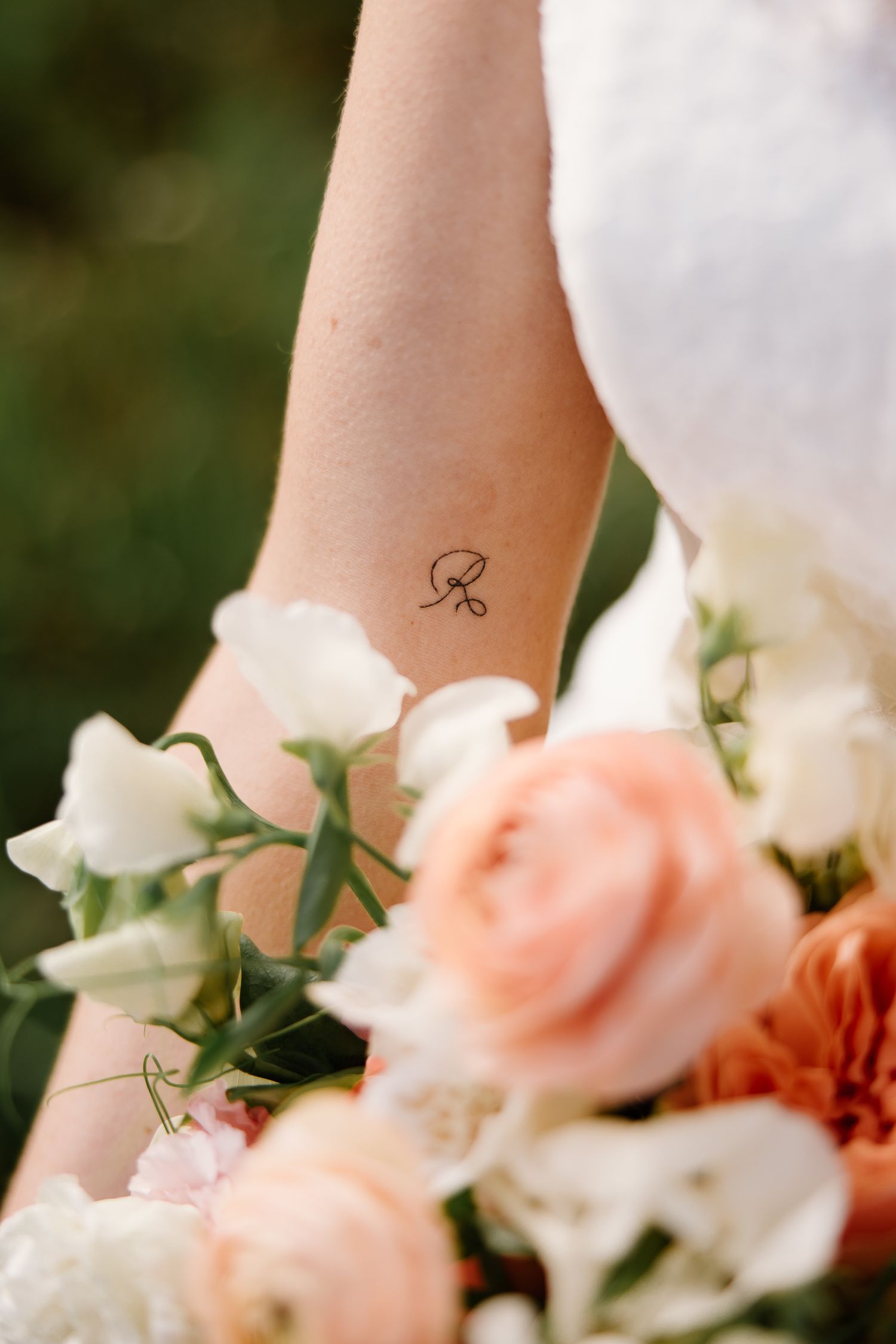 Close-up of bride's arm tattoo beside a bouquet of peach and white roses at a wedding.