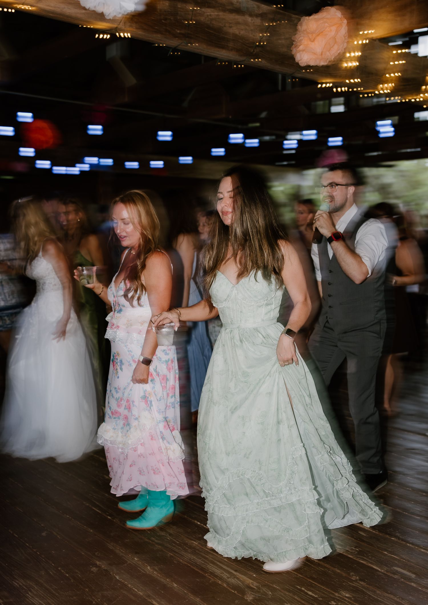 Guests in formal dresses dance energetically on the wooden dance floor at a lively wedding reception.