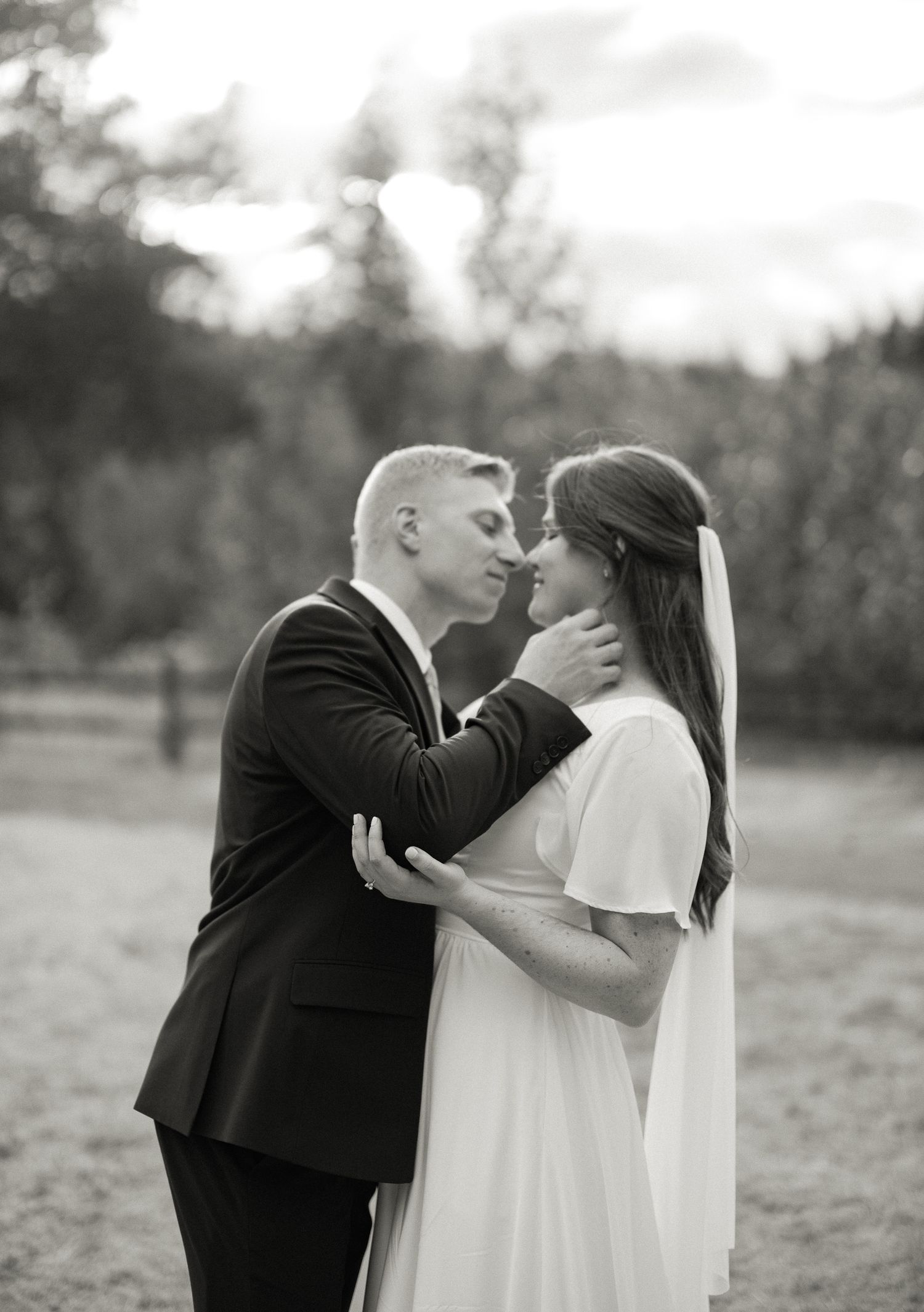 Black and white photo of a bride and groom sharing a romantic moment outdoors on their wedding day.