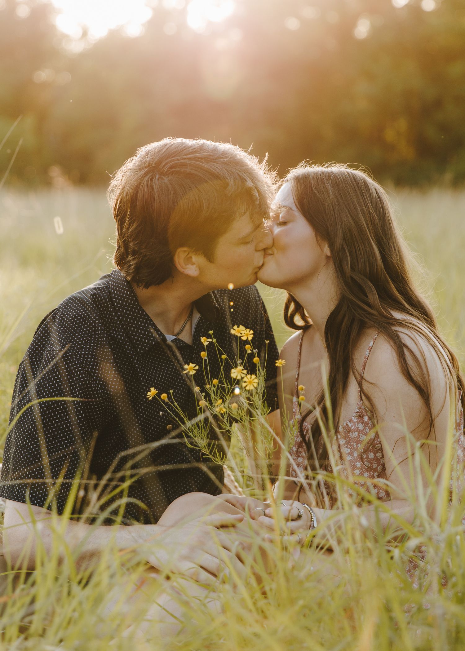 Couple kissing among wildflowers in a sun-drenched meadow during golden hour.