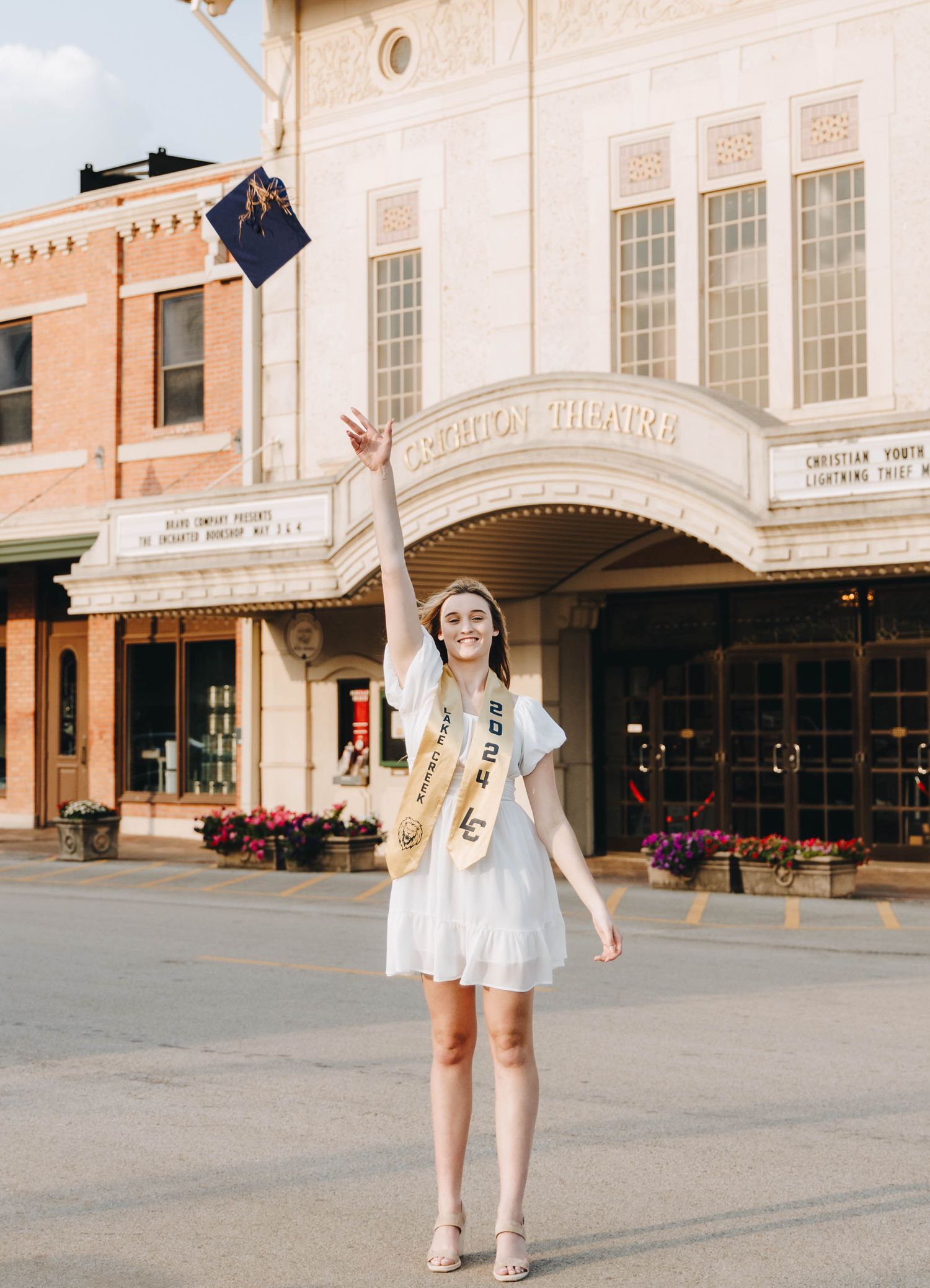 Smiling graduate tossing cap in front of historic Criterion Theatre in joyful senior graduation portrait.