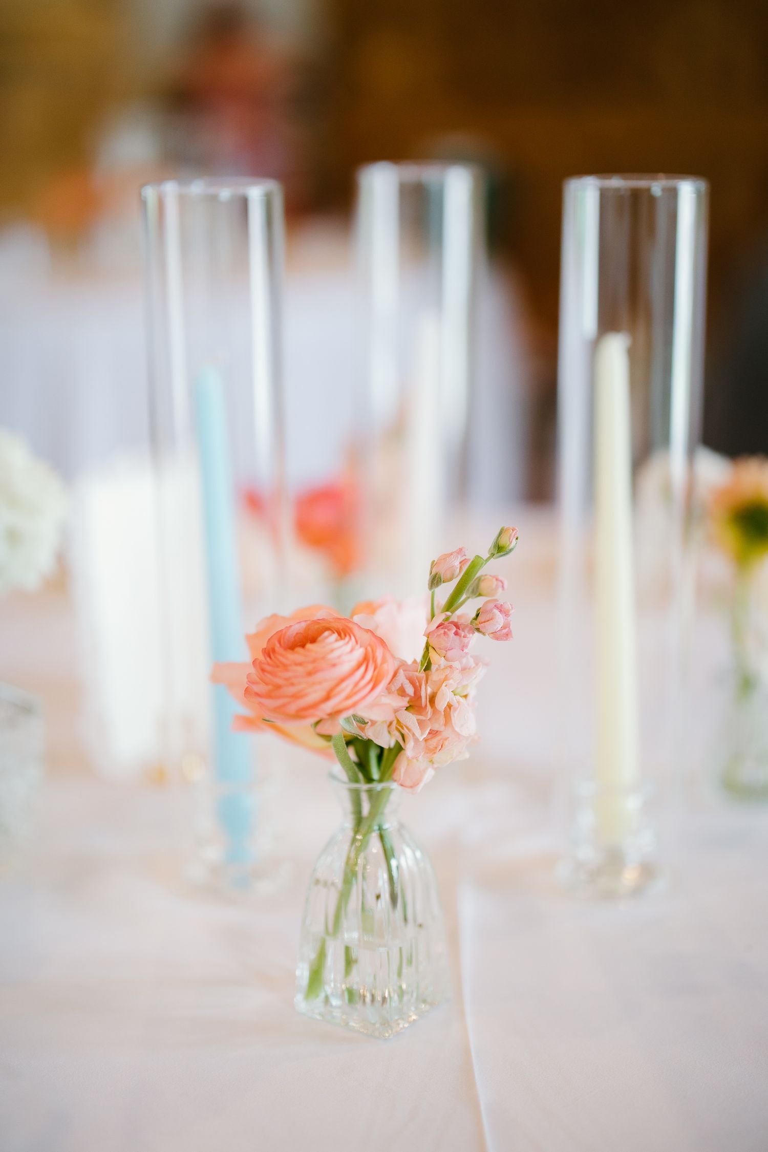 Elegant wedding reception table with peach ranunculus in glass bud vase and pastel taper candles.