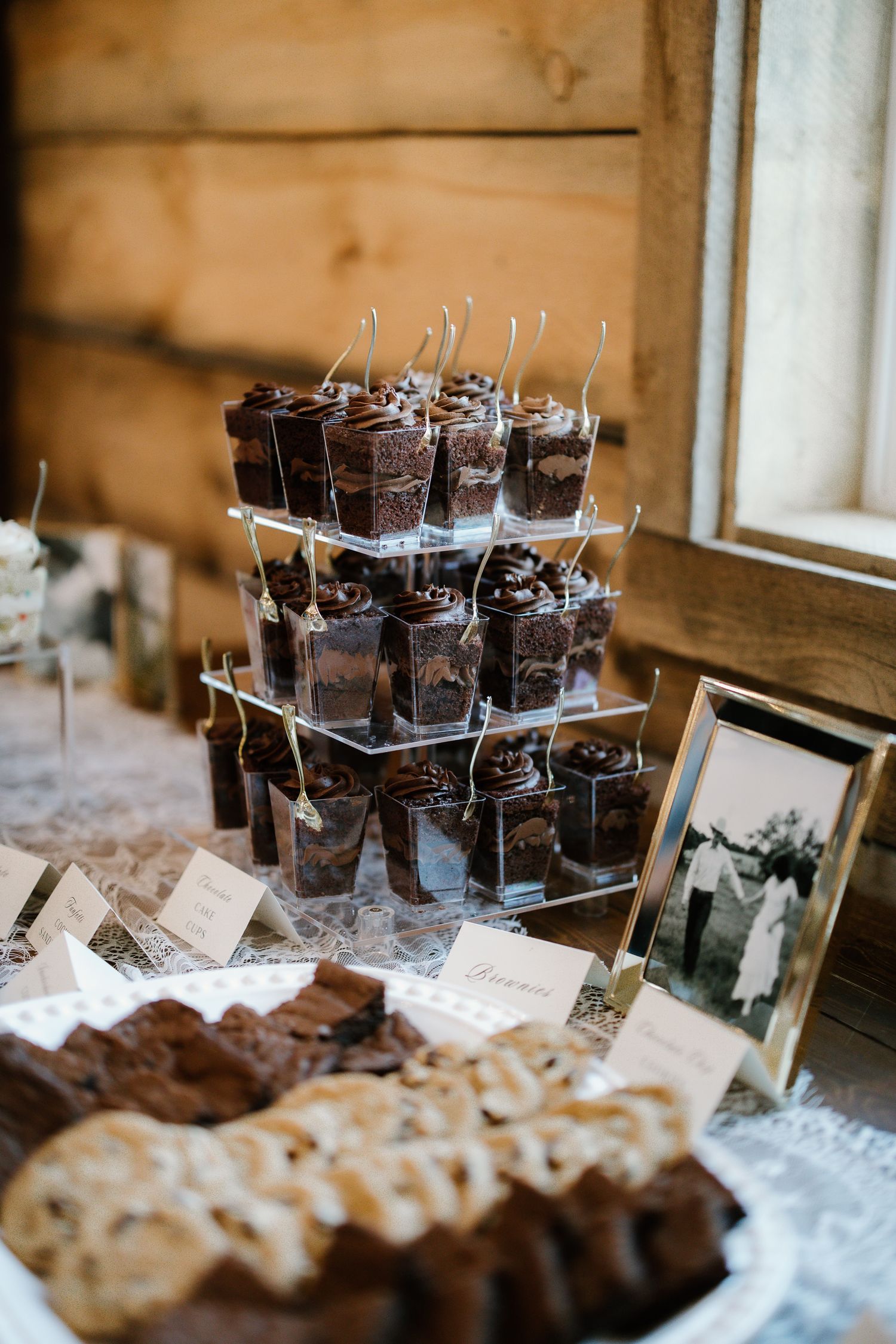 Rustic wedding dessert table with chocolate cup cakes on tiered stand brownies and vintage photo.