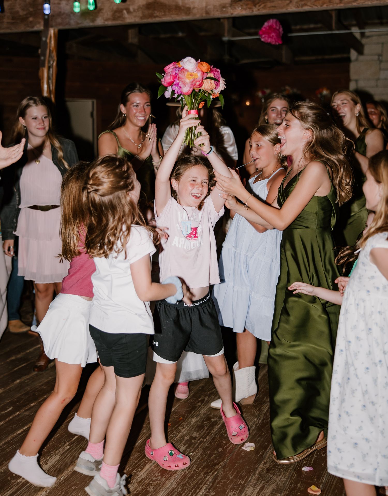 An excited young girl catches the bridal bouquet surrounded by other children and guests on the dance floor.
