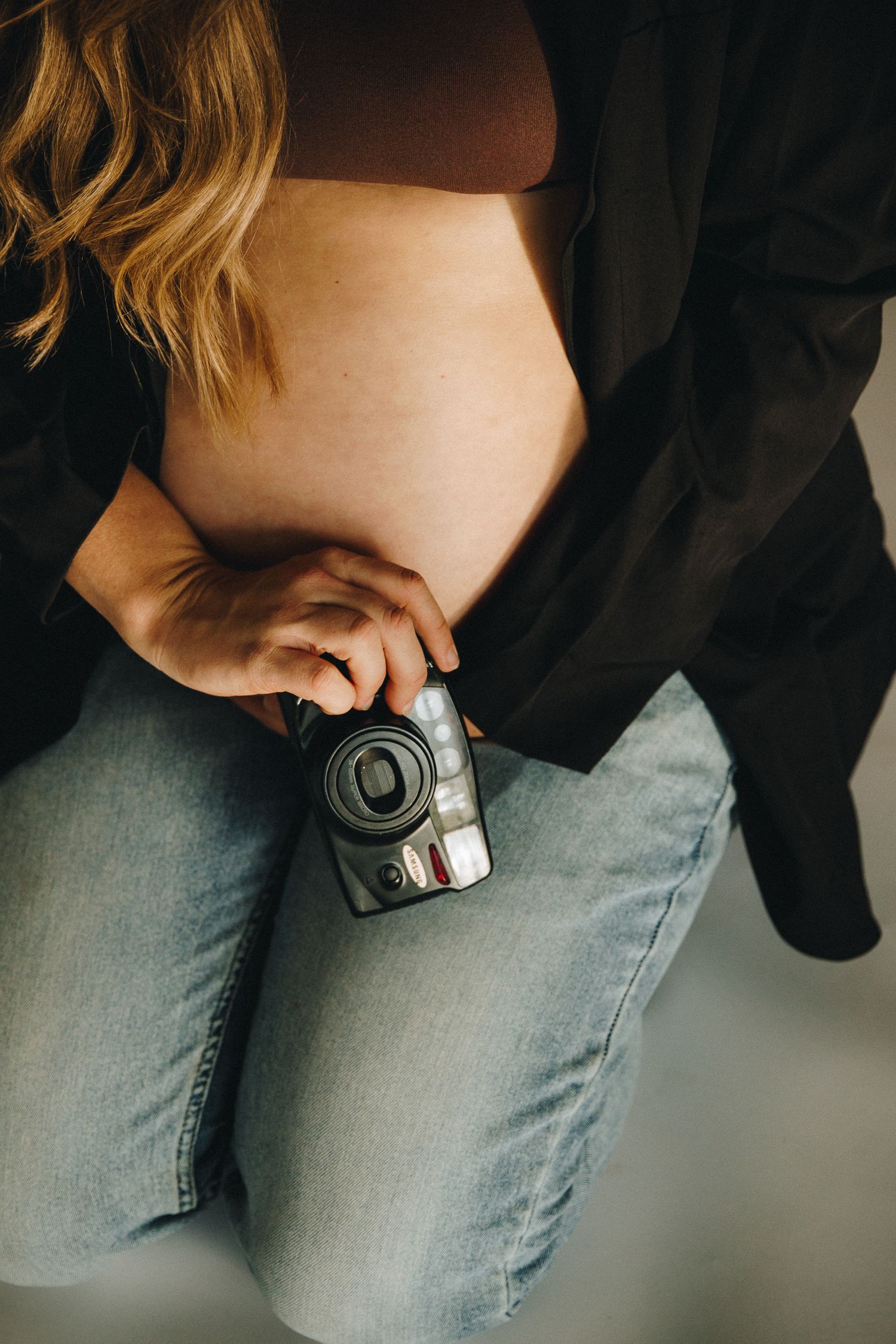 Close-up of pregnant belly with black blazer and jeans holding a vintage camera.