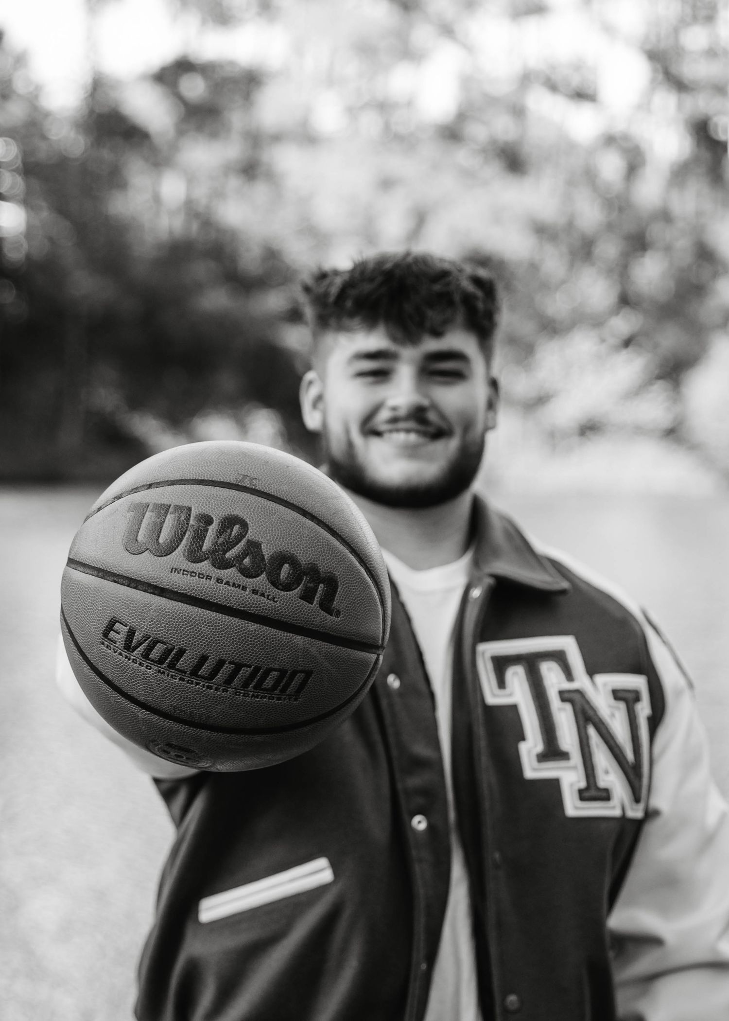 Smiling young man holding a Wilson Evolution basketball toward the camera in black and white.