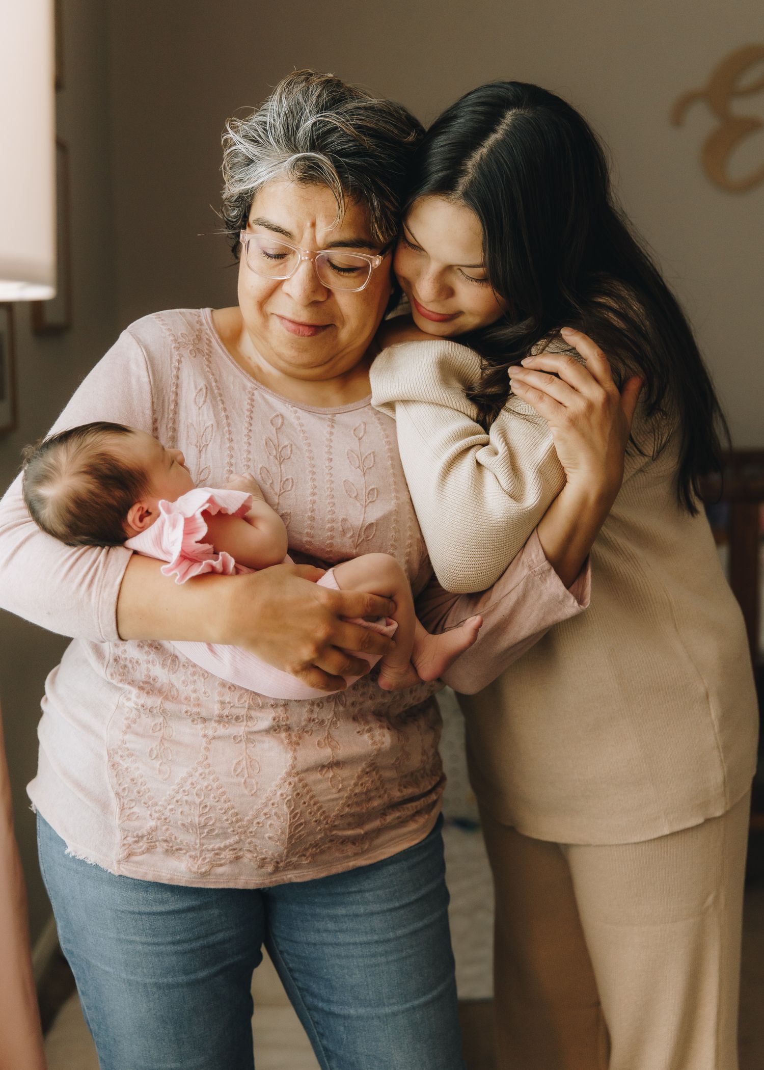 Three generations embrace as grandmother holds newborn baby while mother hugs her warmly.