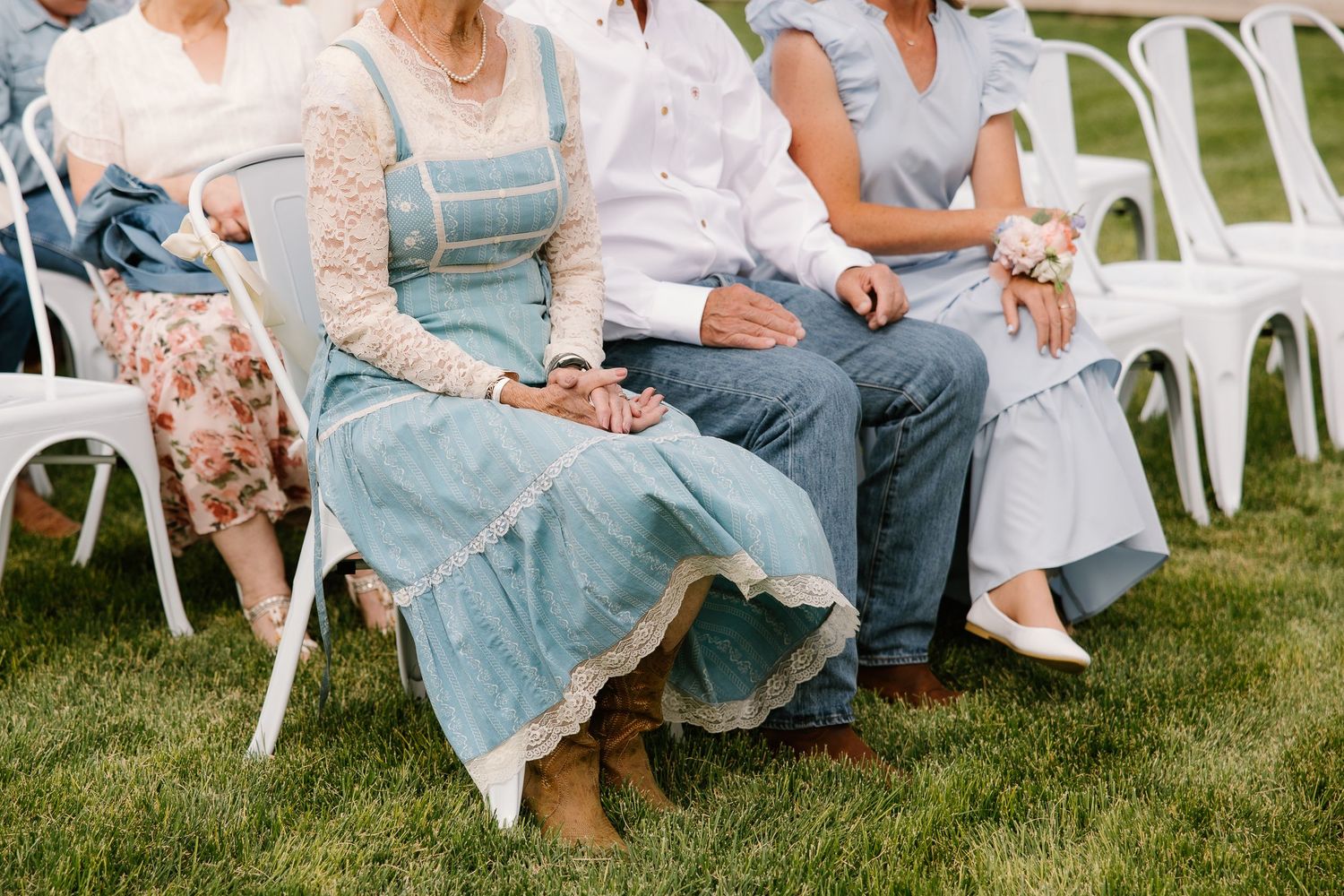 Wedding guests seated in white chairs on green grass during an outdoor rustic wedding ceremony.