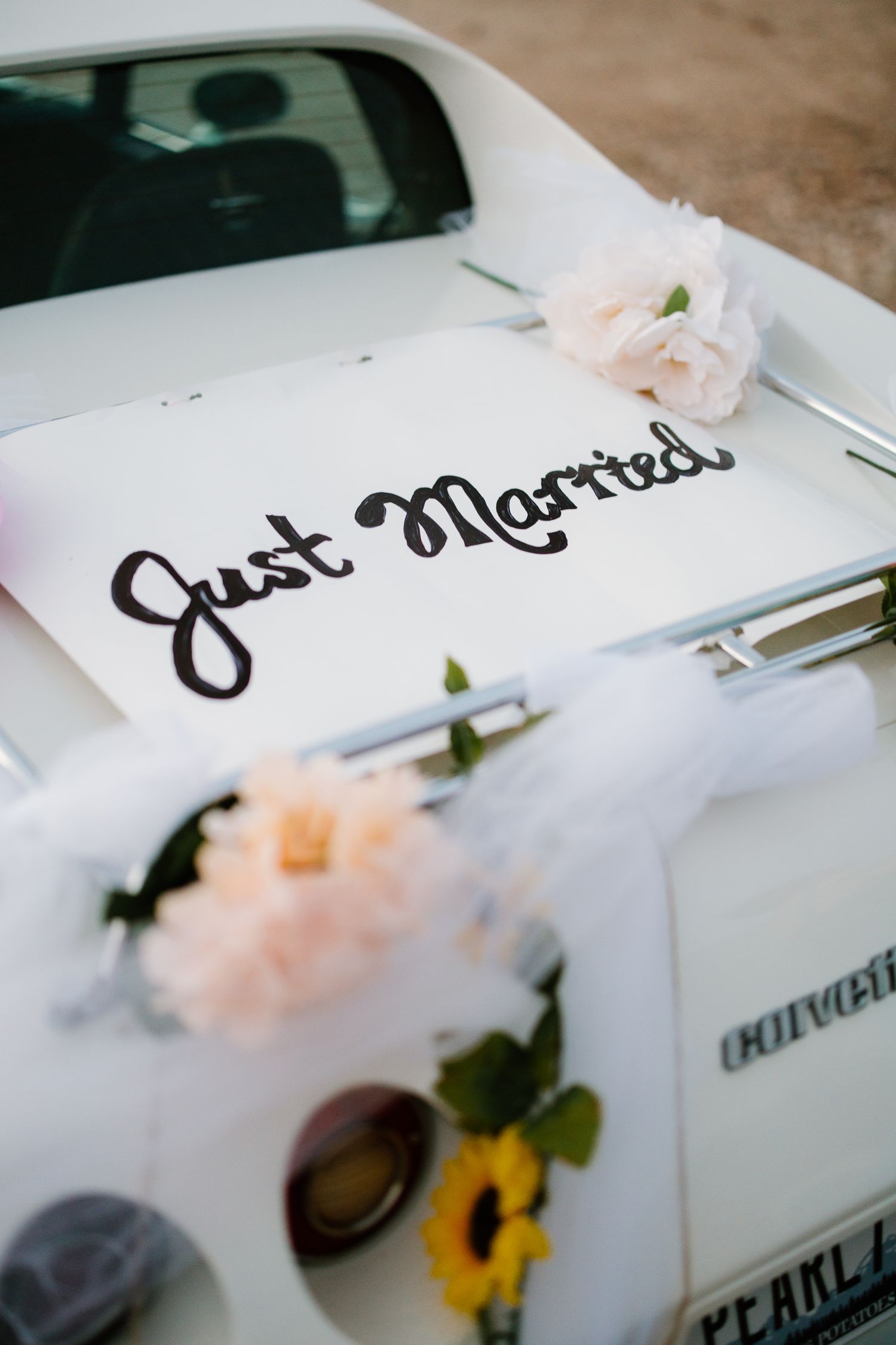 Just Married sign with floral decorations displayed on a white vintage Corvette wedding getaway car.