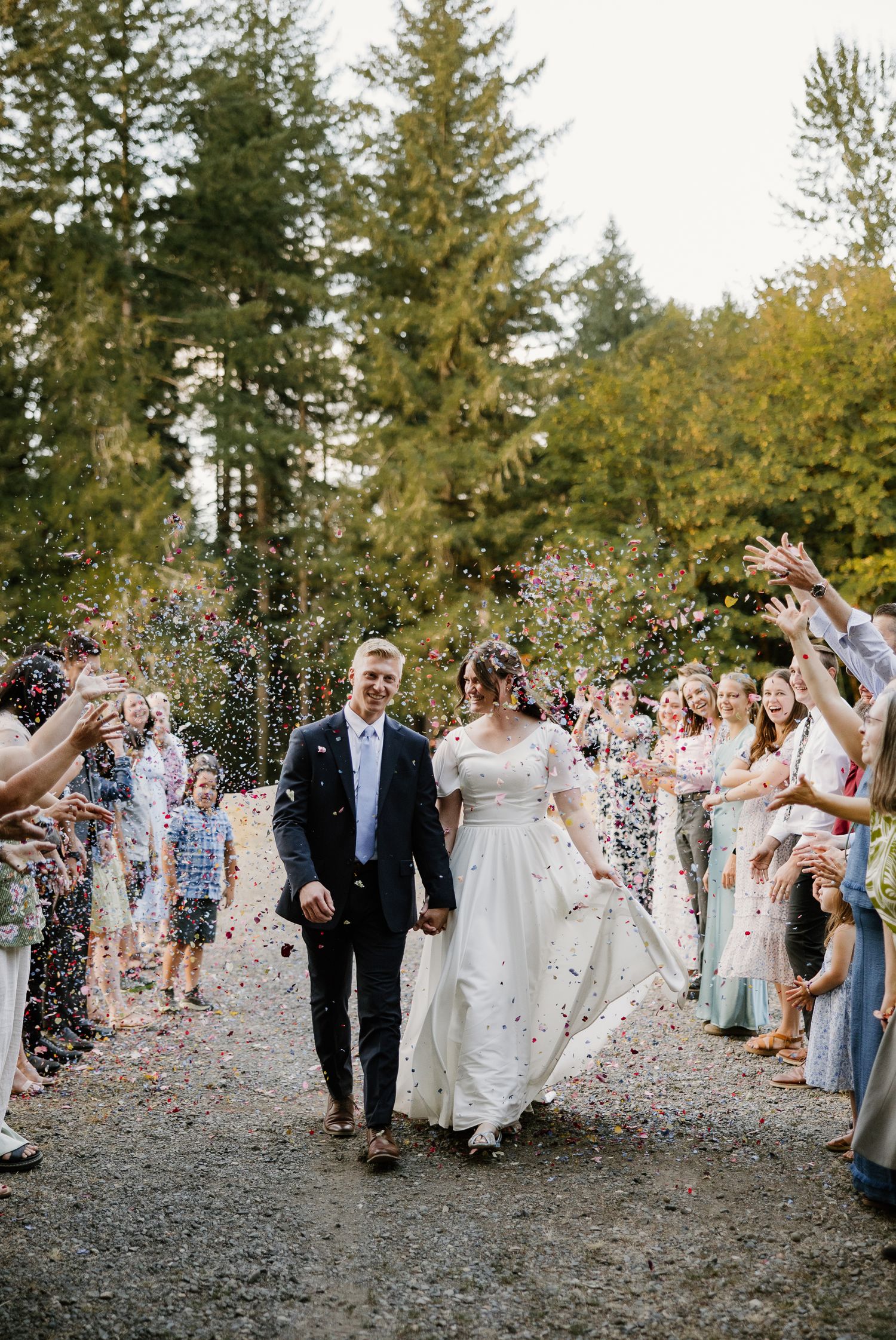 Bride and groom smile joyfully as guests toss confetti during their outdoor wedding grand exit.