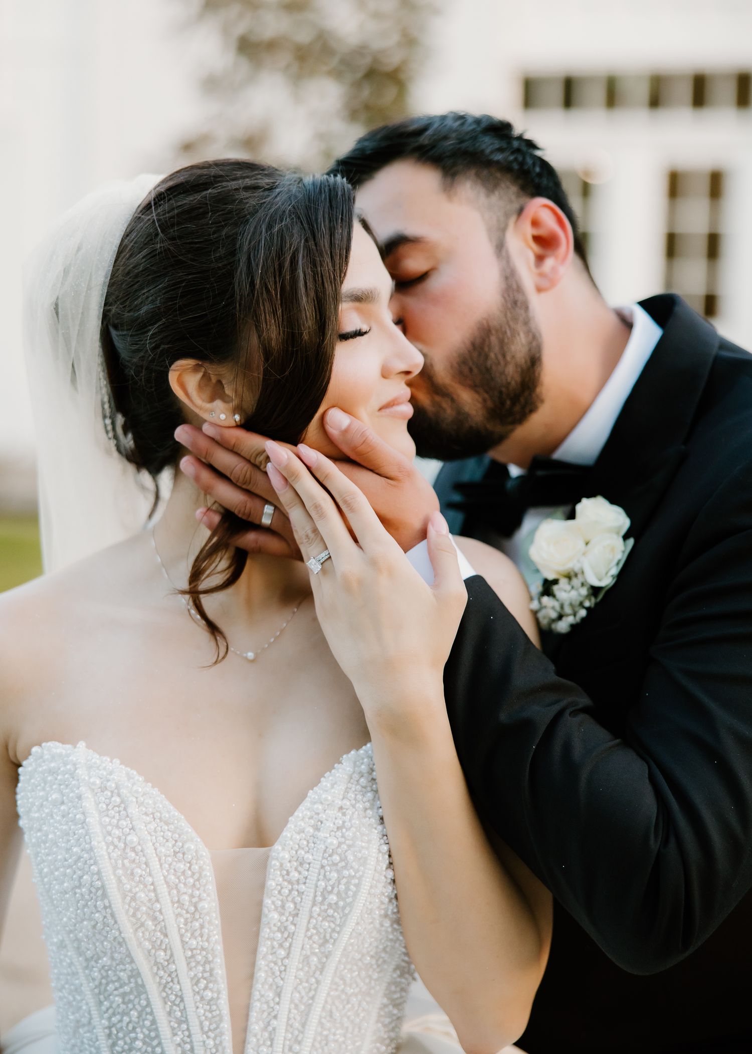 Groom tenderly kisses bride on cheek while cradling her face during romantic wedding portrait.