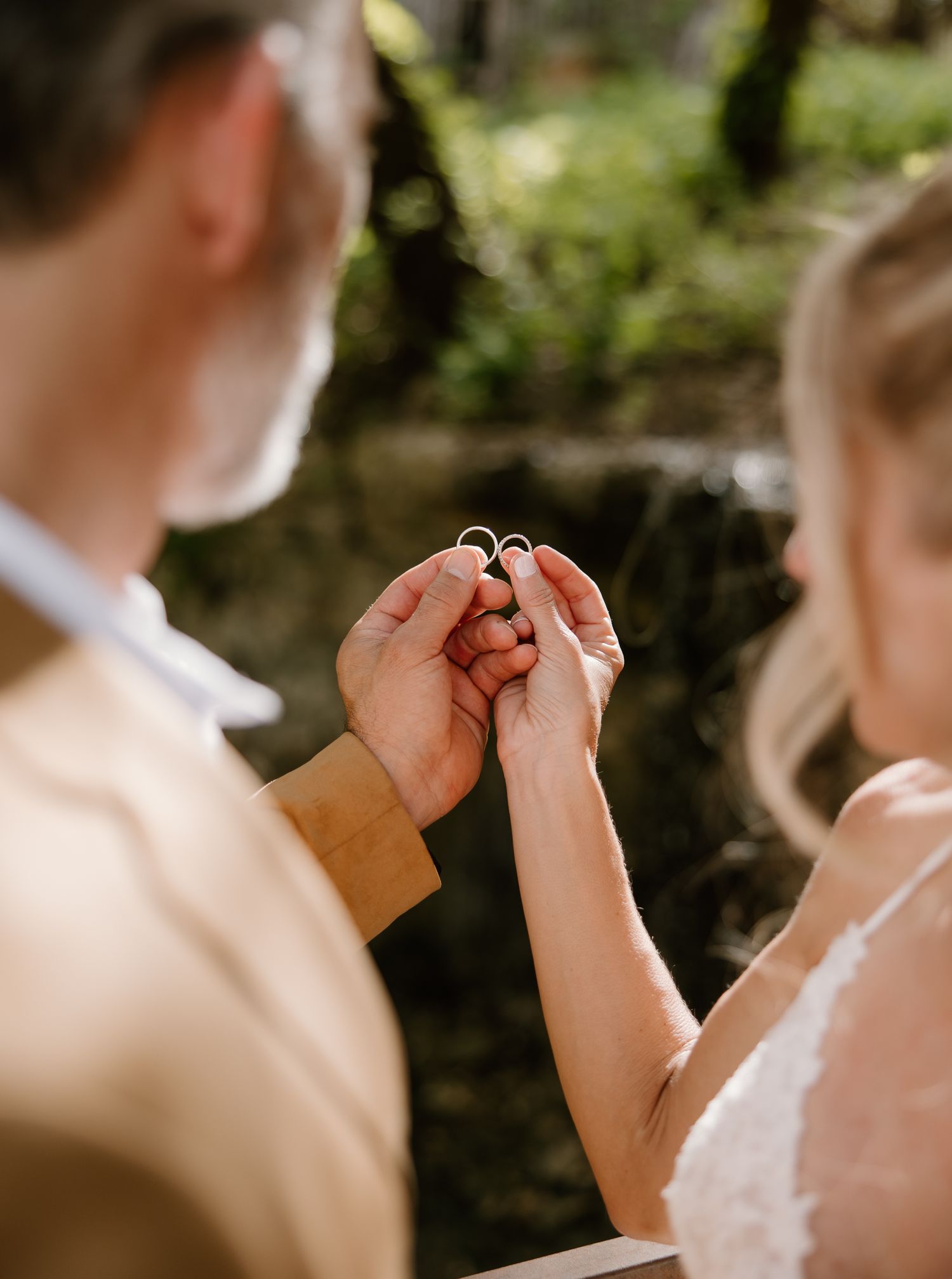 Couple holding two wedding rings together outdoors during a romantic forest elopement ceremony.