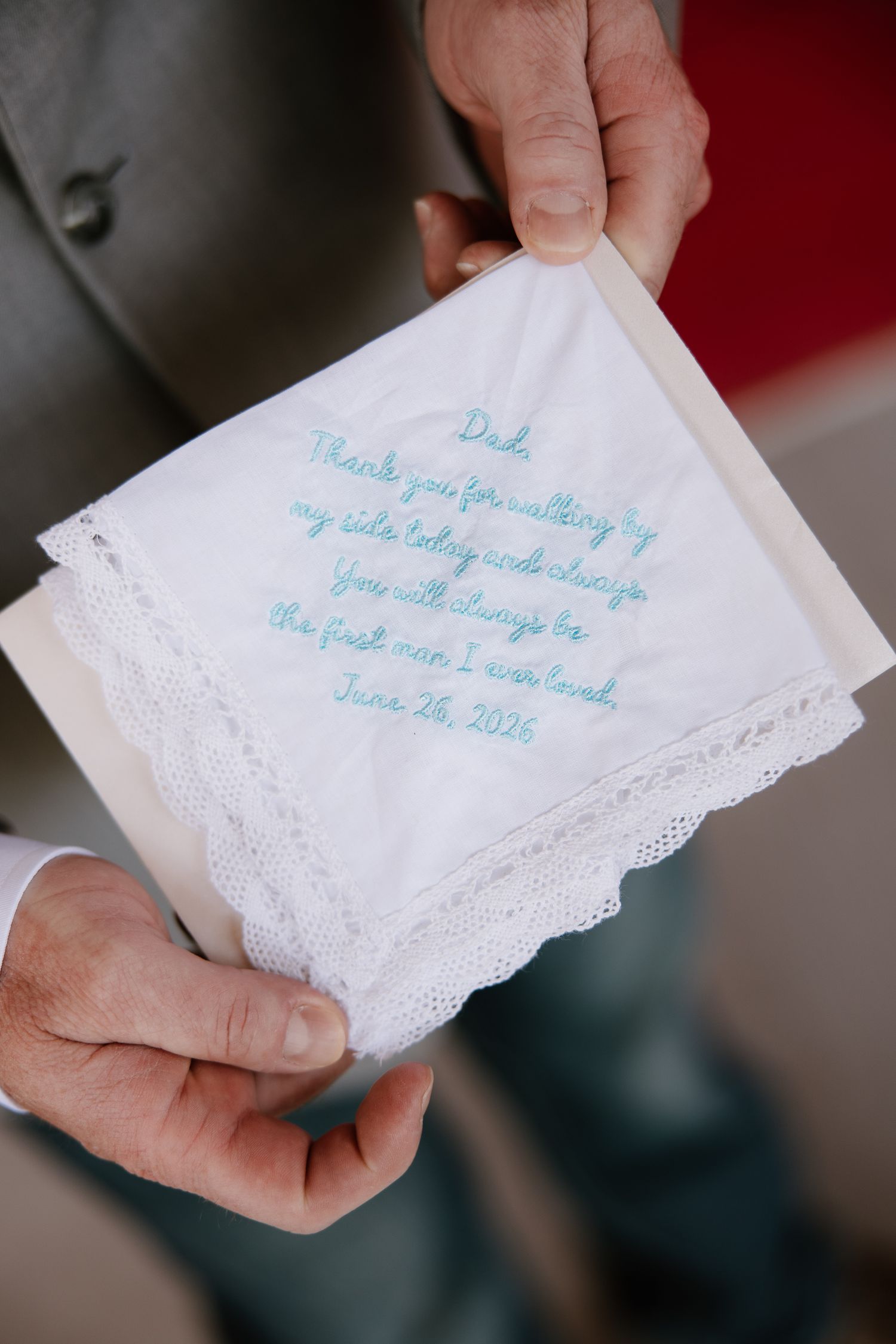 Father of the bride holds embroidered handkerchief wedding gift with heartfelt blue stitched message.
