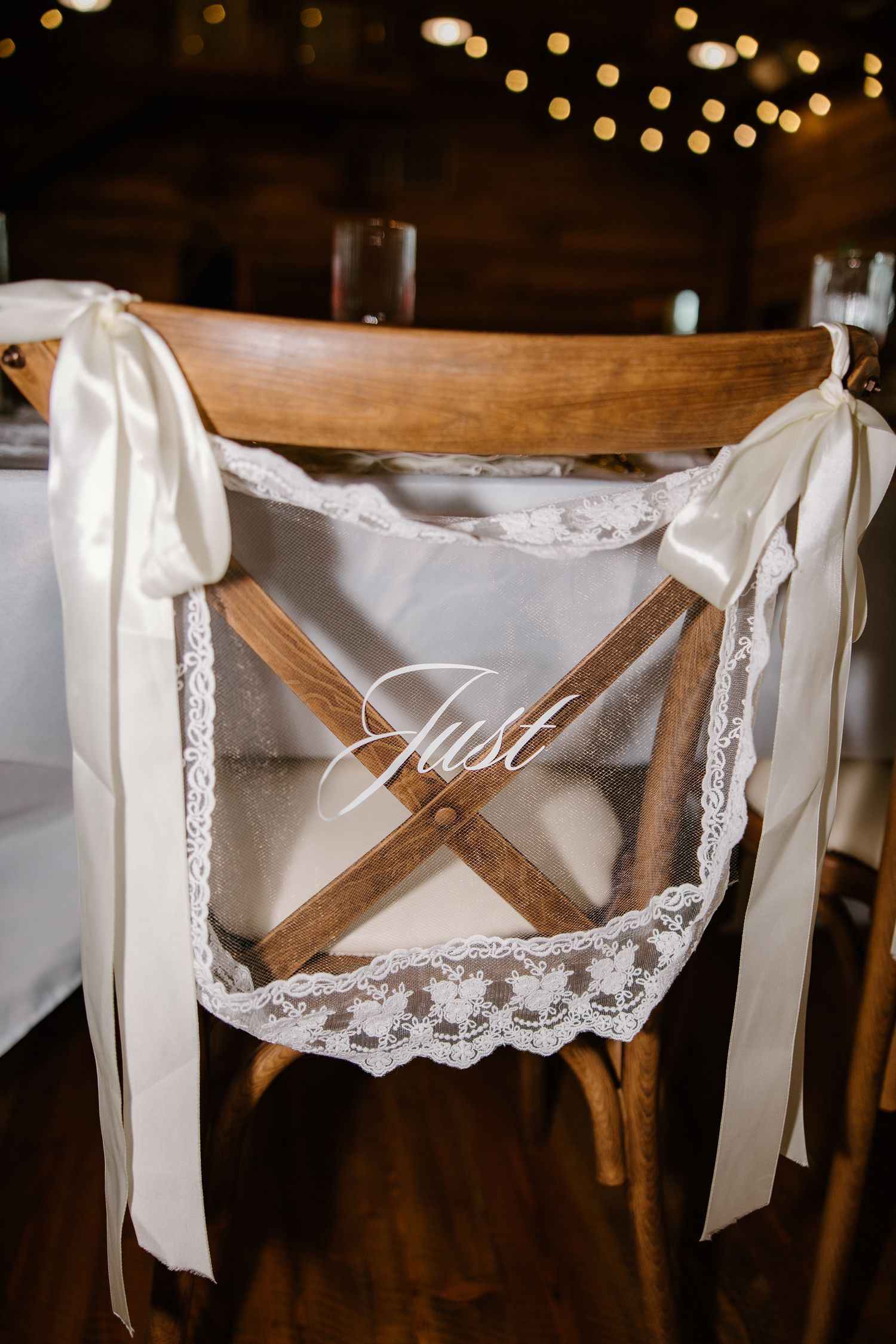Rustic wooden wedding chair decorated with white lace and ribbon bows displaying a cursive Just married sign.