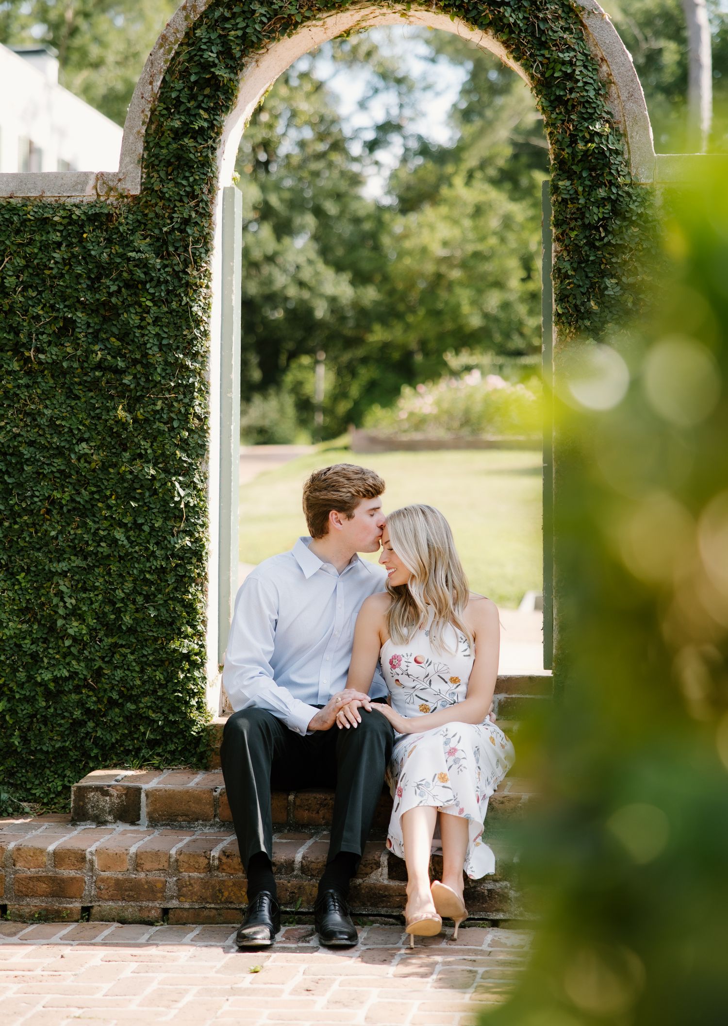 Couple sharing a kiss seated in an ivy-covered stone archway in a garden.