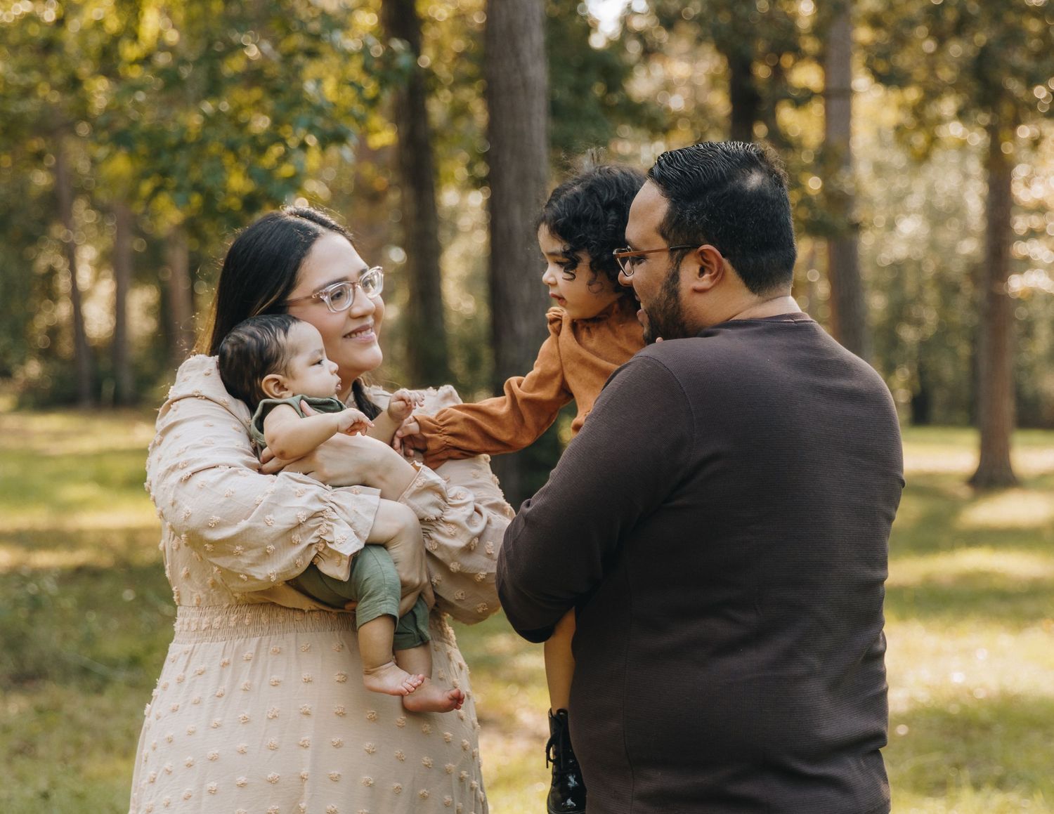 Happy South Asian family with two young children share a joyful moment in a sunny park.