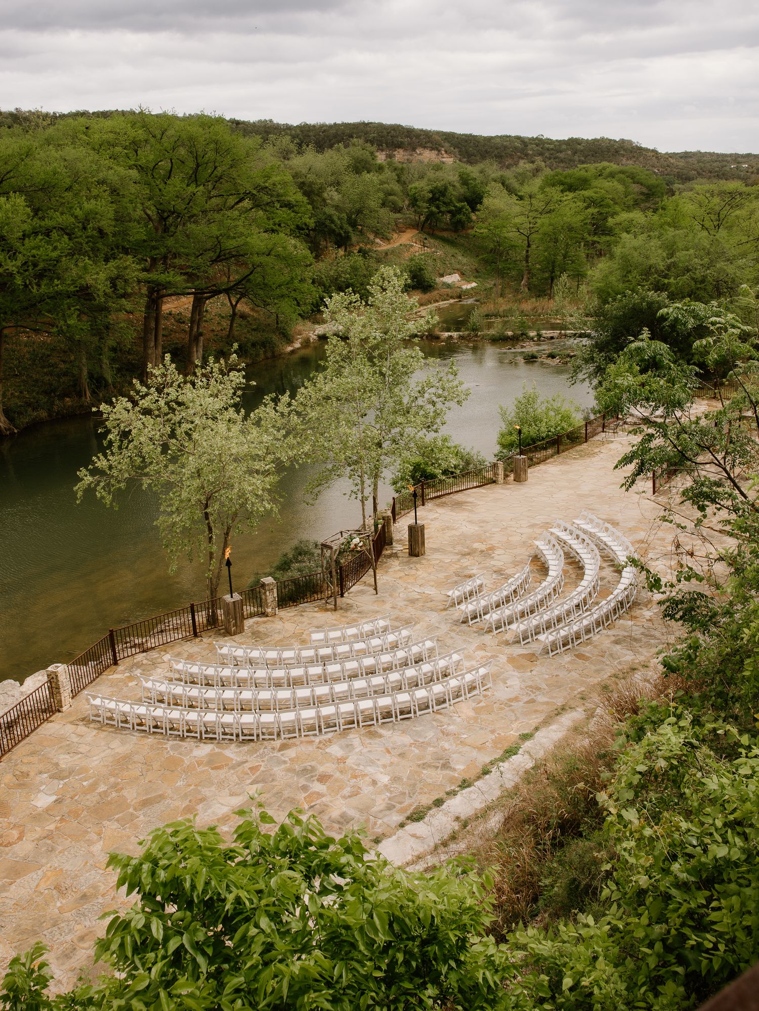 Outdoor wedding ceremony setup with white chairs by a scenic river and lush greenery.