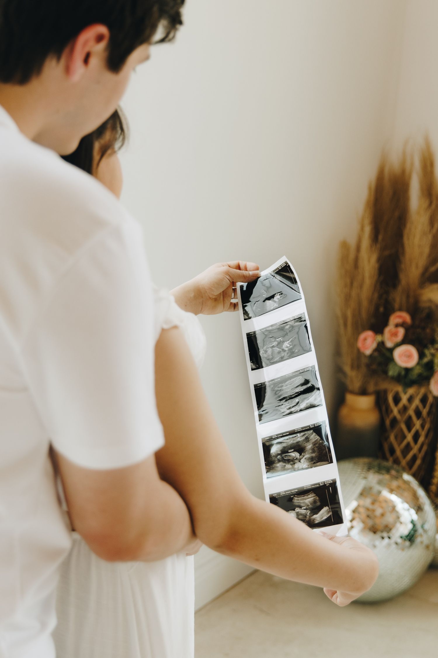 Couple reviewing ultrasound photos together in a softly lit room with dried floral decor.