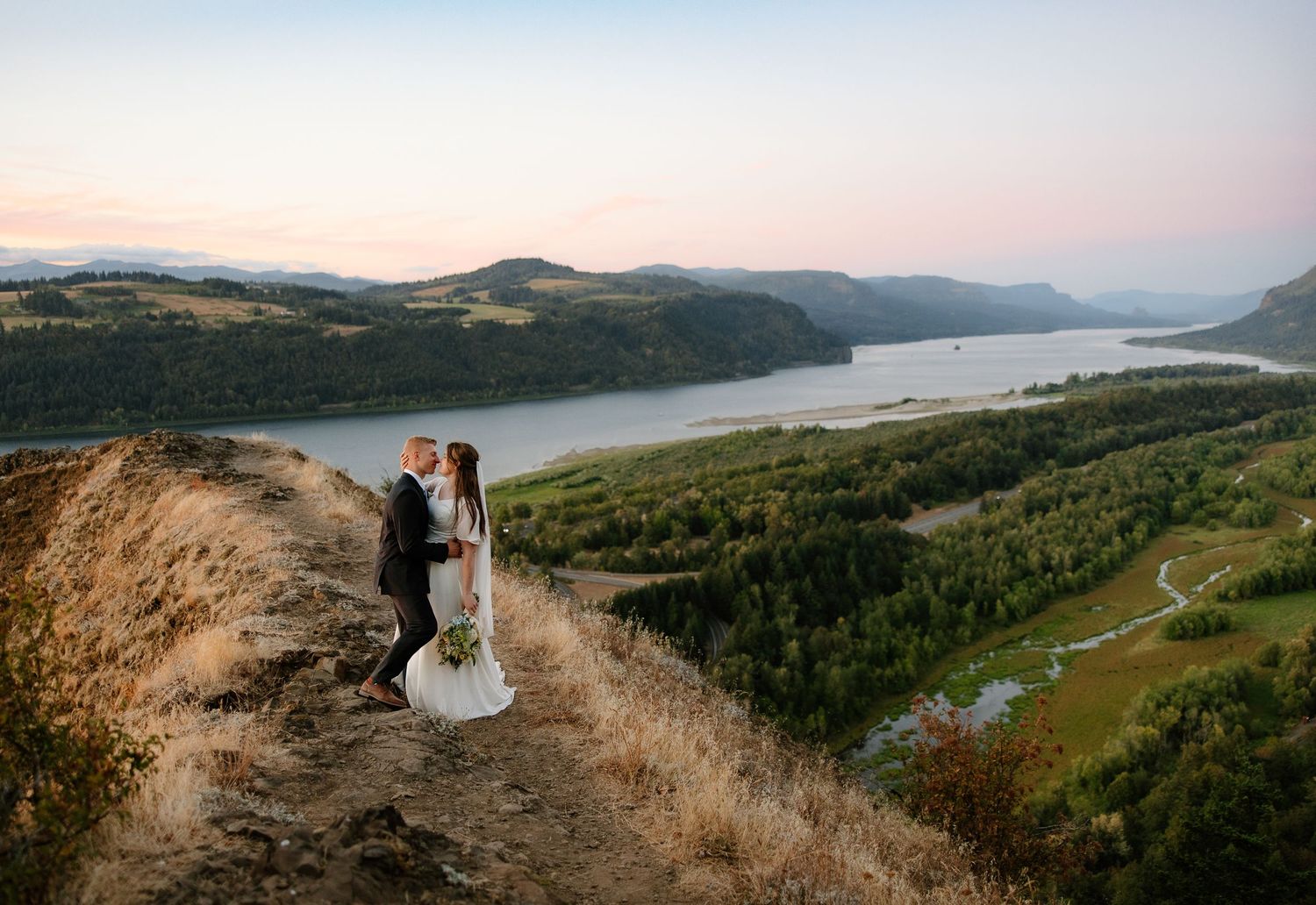 Couple embraces on a hilltop at sunset overlooking the Columbia River Gorge in a stunning wedding photo.