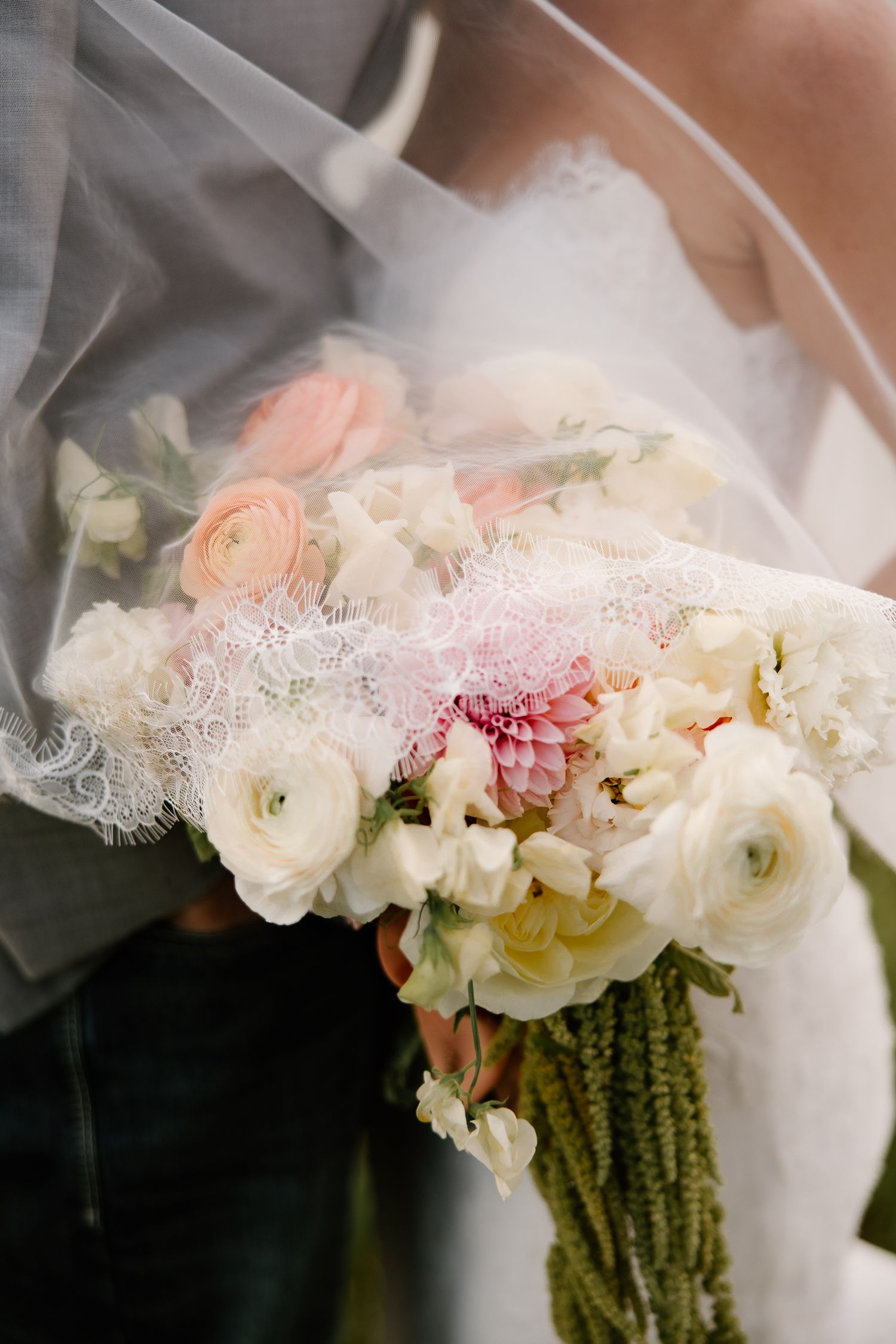 Close-up of bridal bouquet with pink dahlias, ranunculus, and white roses draped with lace veil.