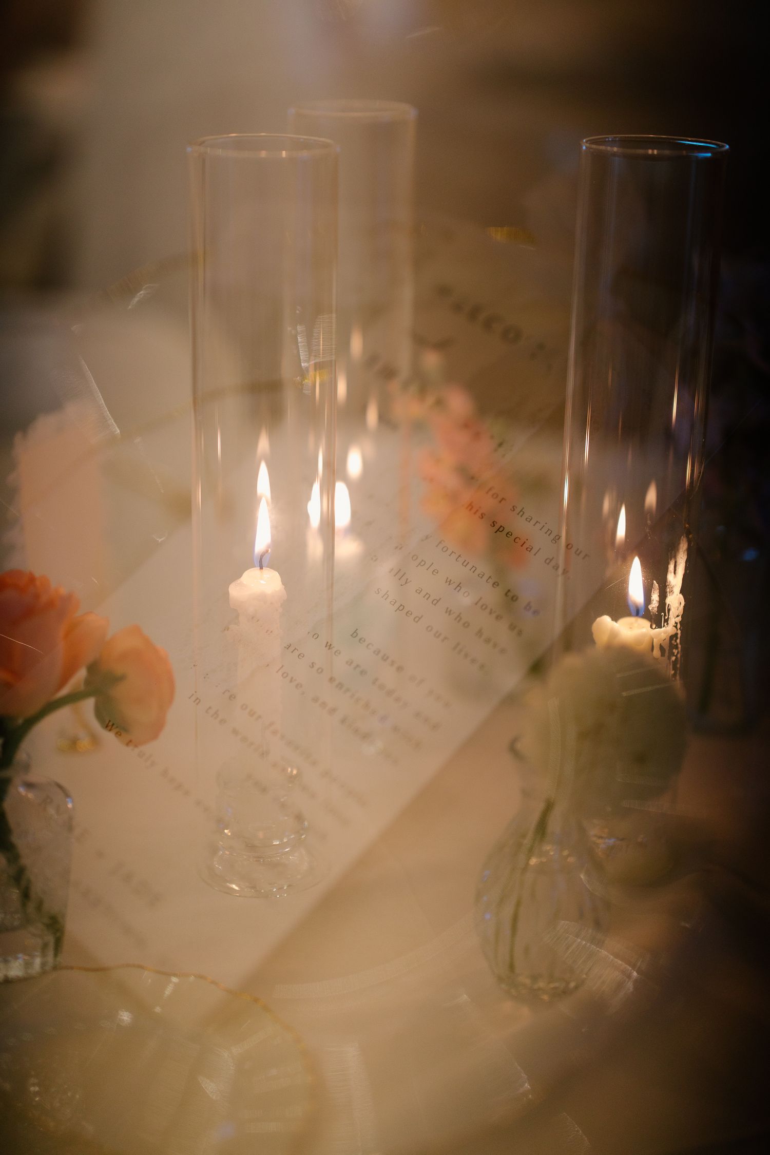 Romantic wedding table setting with tall glass candle holders, lit candles, and elegant menu cards among florals.