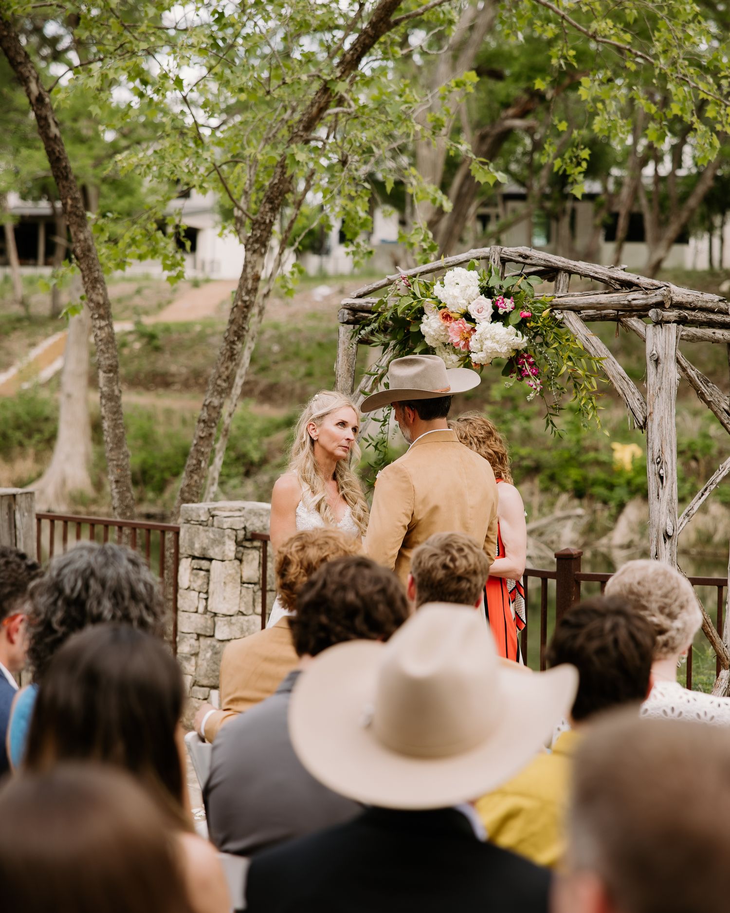 Couple exchanging vows under floral rustic arch at outdoor wedding.
