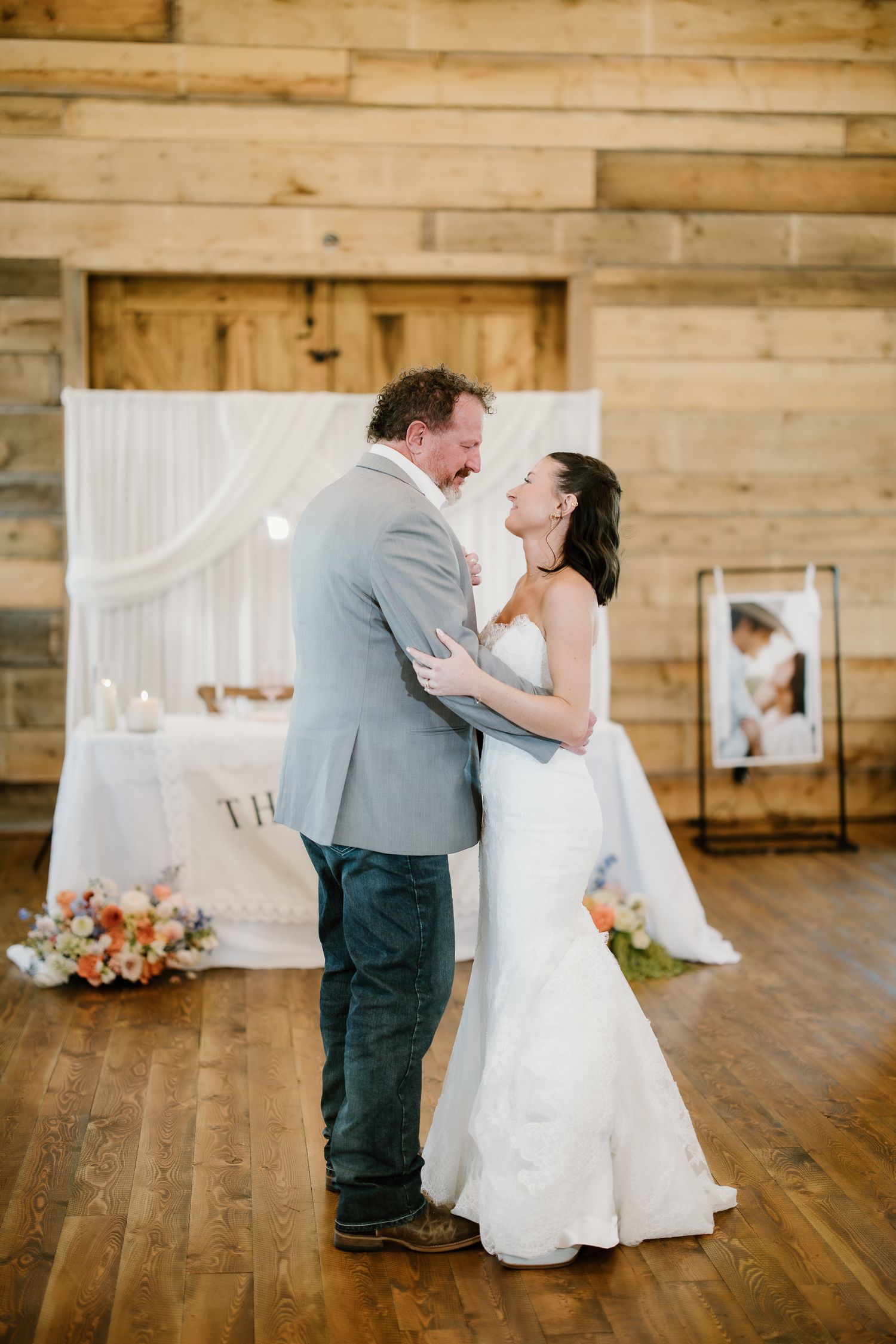 Bride and groom sharing joyful first dance in rustic barn reception with white drape backdrop.