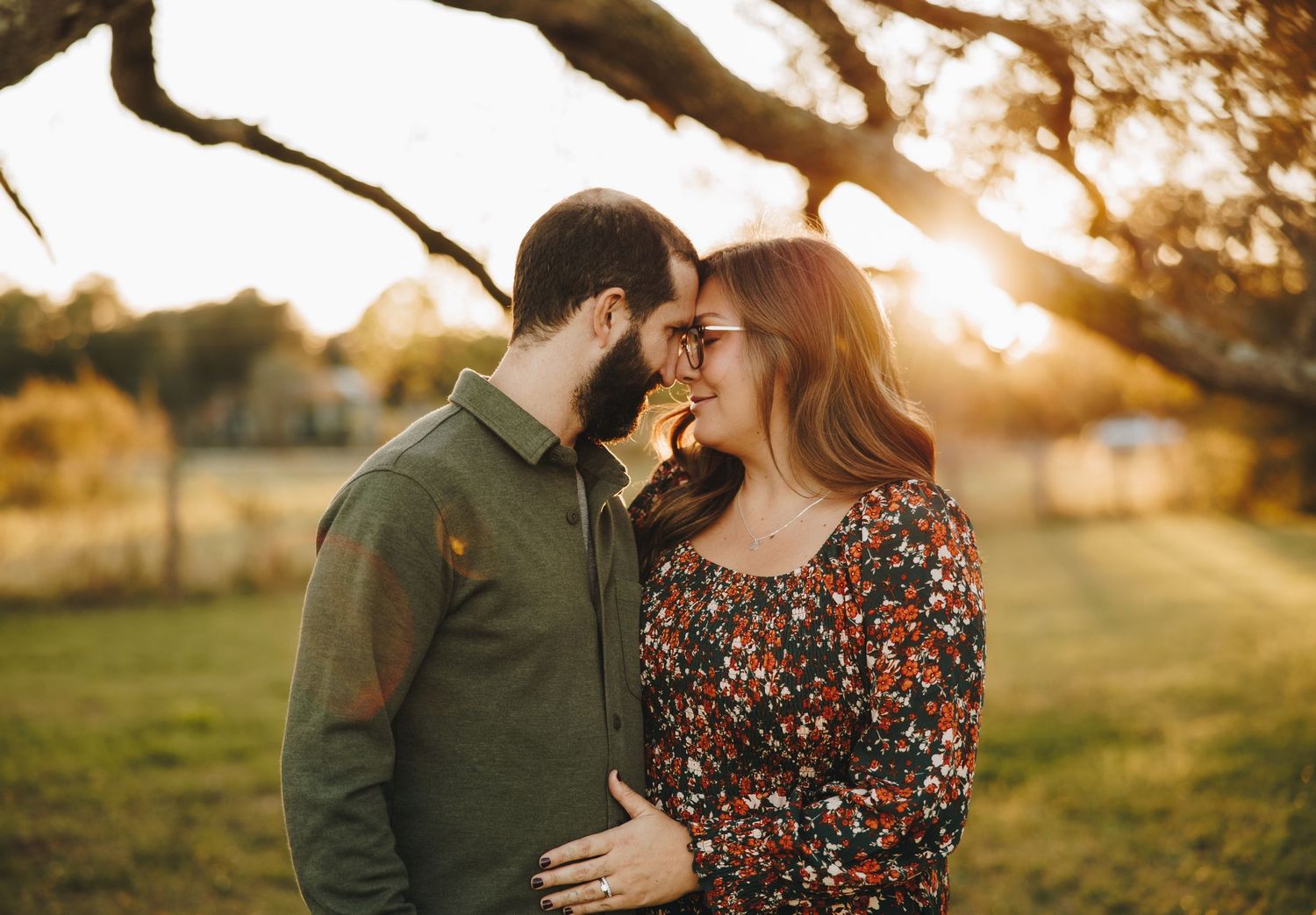 Couple sharing a romantic moment at golden hour under a large tree in a park.