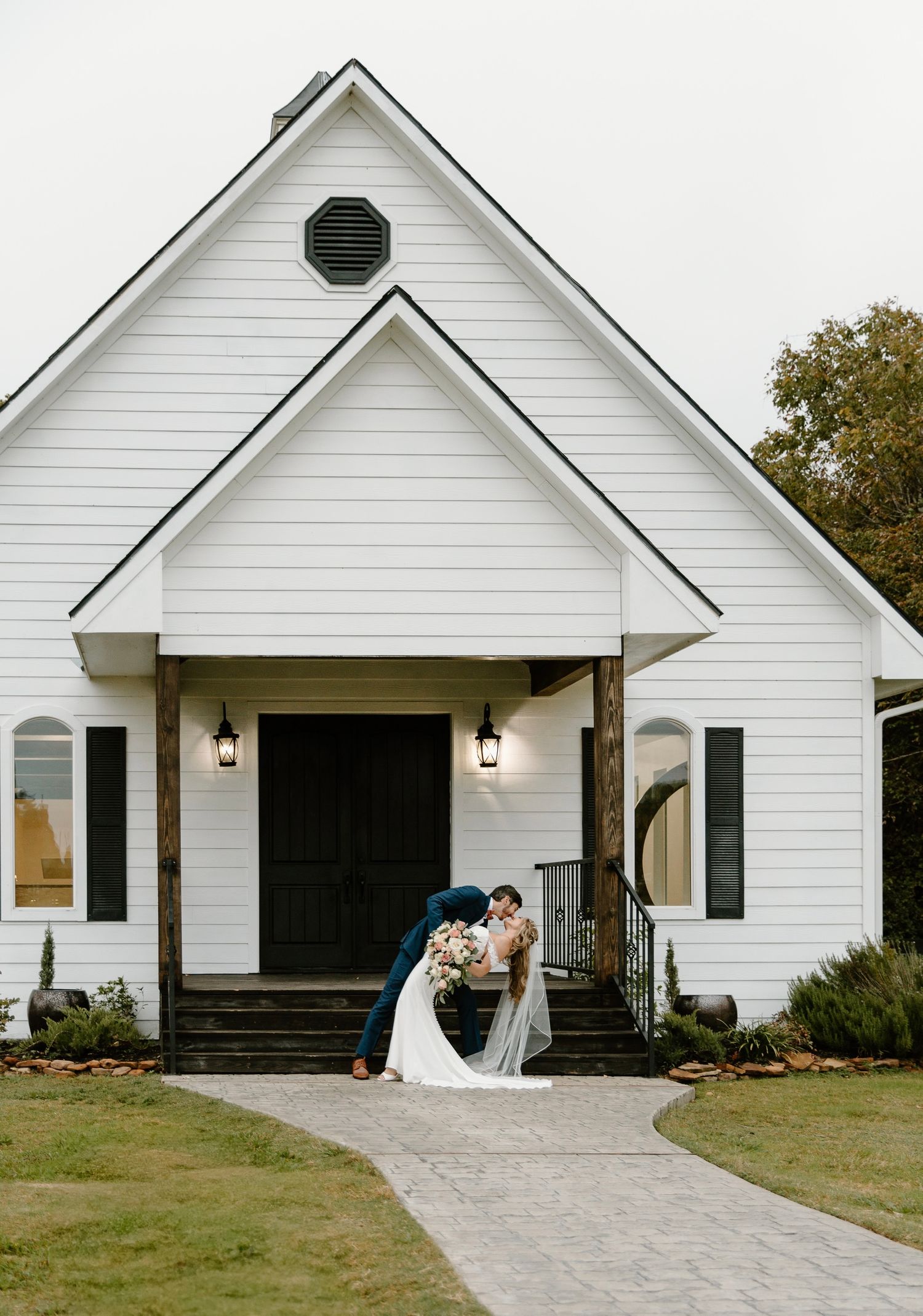 Bride and groom sharing a romantic dip kiss in front of a white chapel wedding venue.