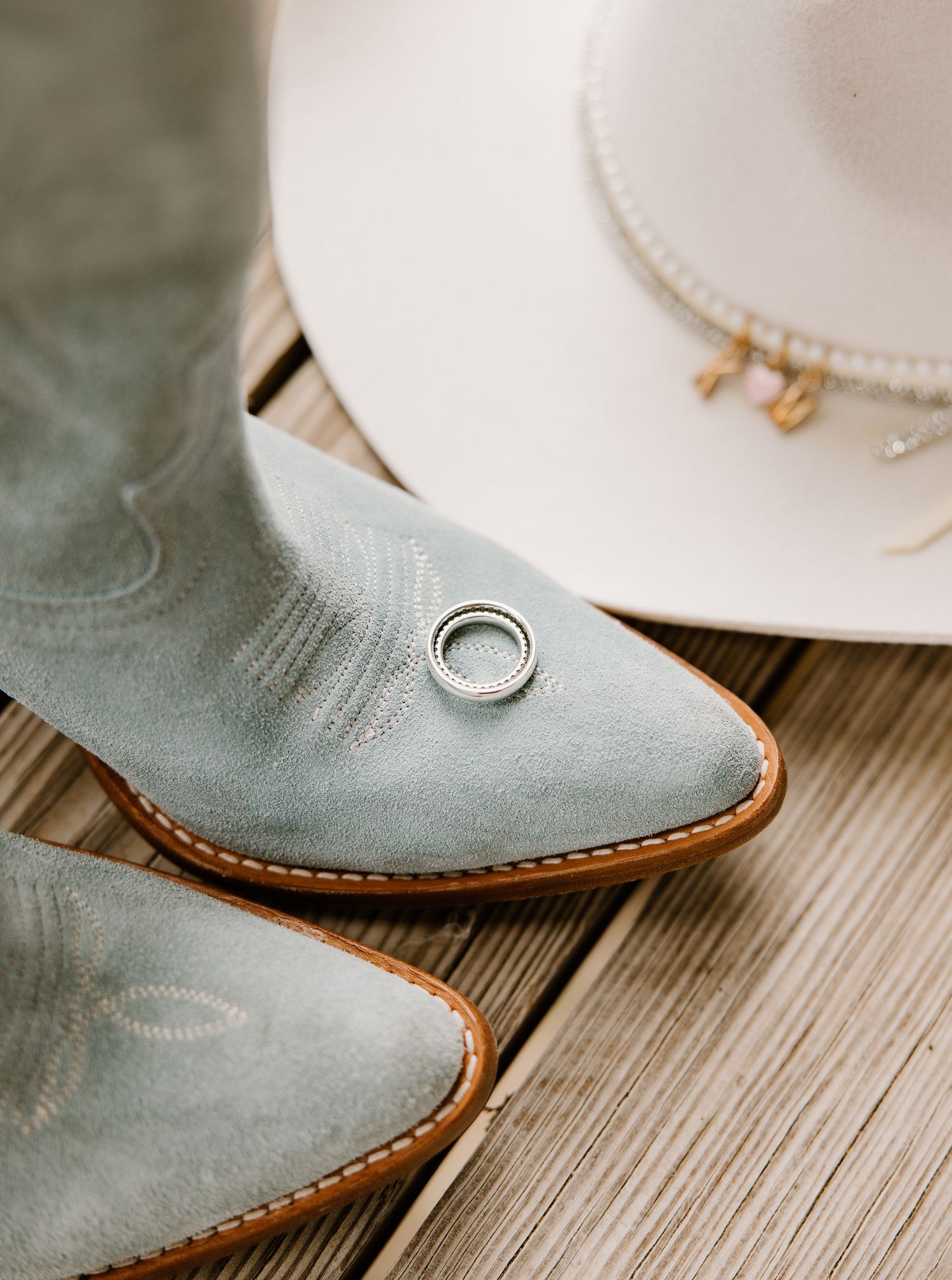 Light blue cowboy boots and white hat with a silver wedding ring on rustic wood planks.