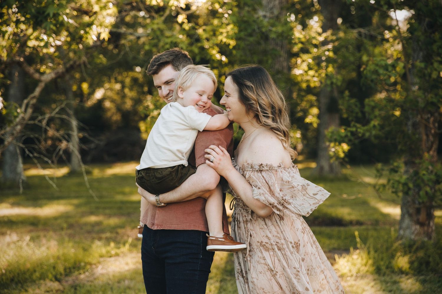 Young couple lovingly holding their smiling toddler in a beautiful green park.
