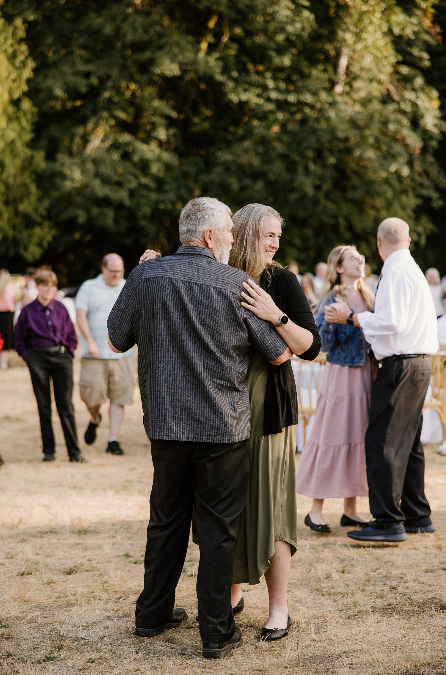 Couple shares a dance outdoors at a wedding reception surrounded by other guests on a sunny day.