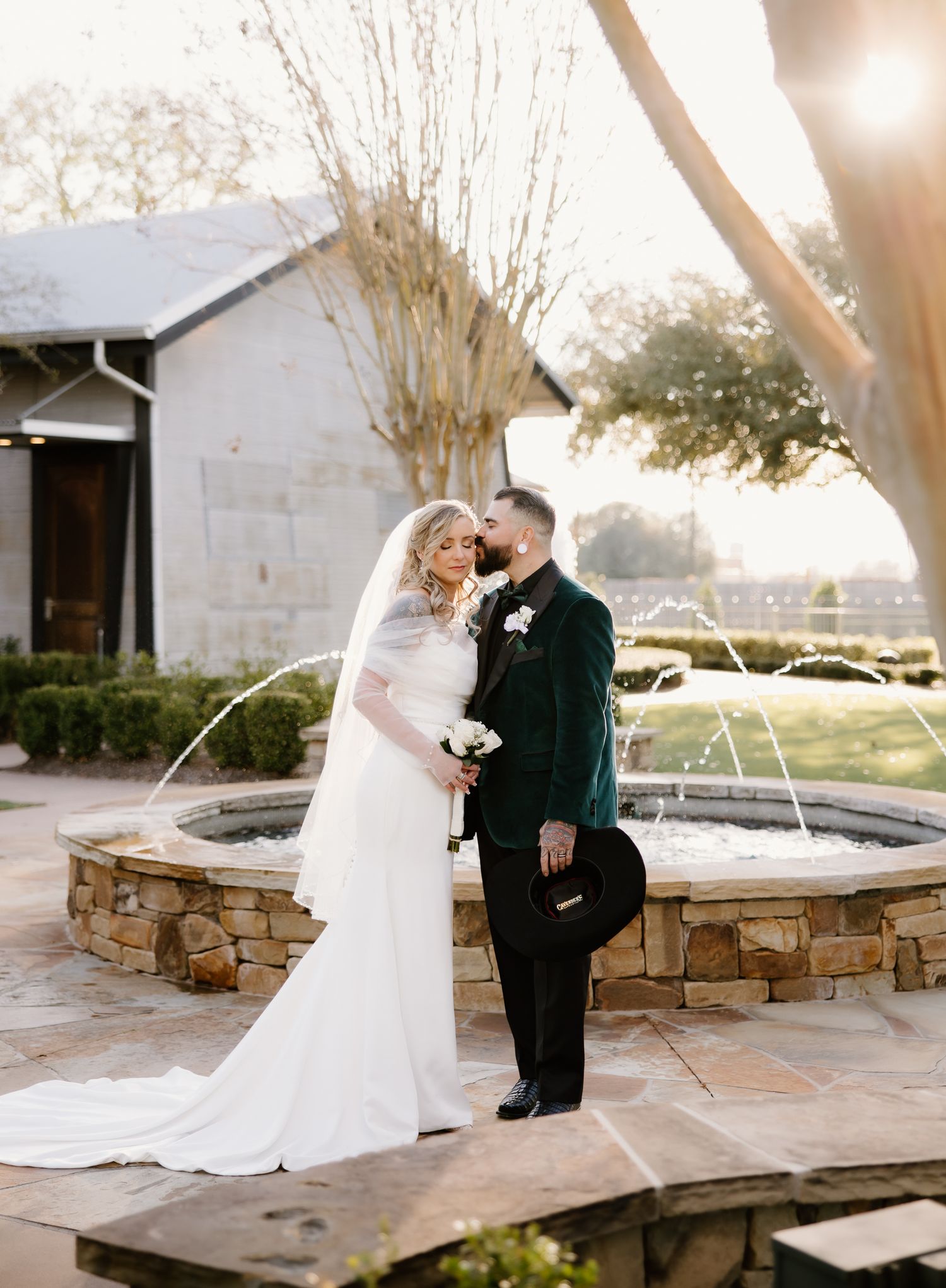 Bride and groom sharing a romantic moment by a stone fountain at golden hour wedding venue.