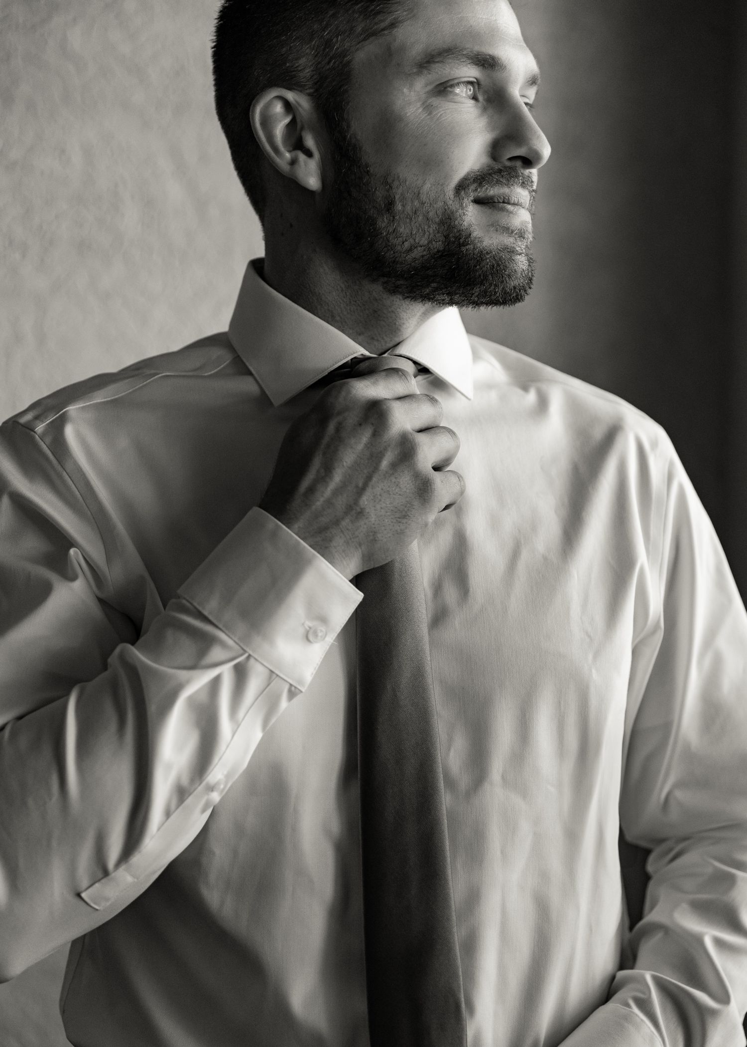 Black and white portrait of groom adjusting tie while getting ready for wedding.