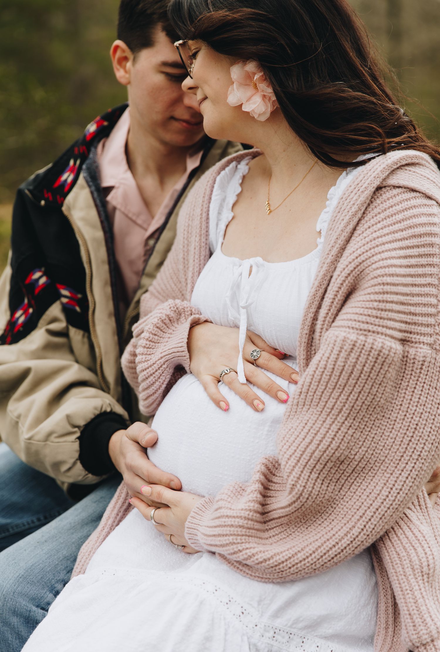 Close-up of couple tenderly holding pregnant belly during outdoor maternity session in pink cardigan.