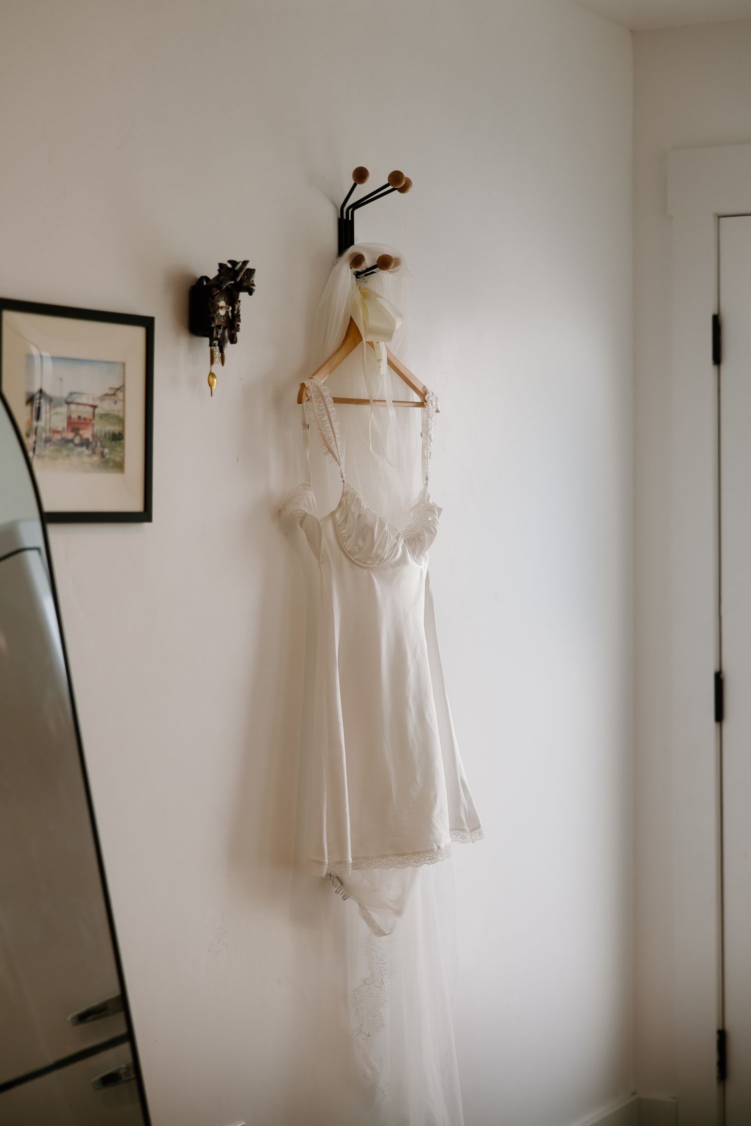 Wedding dress and veil hanging on wall hook in bright white room before the ceremony.
