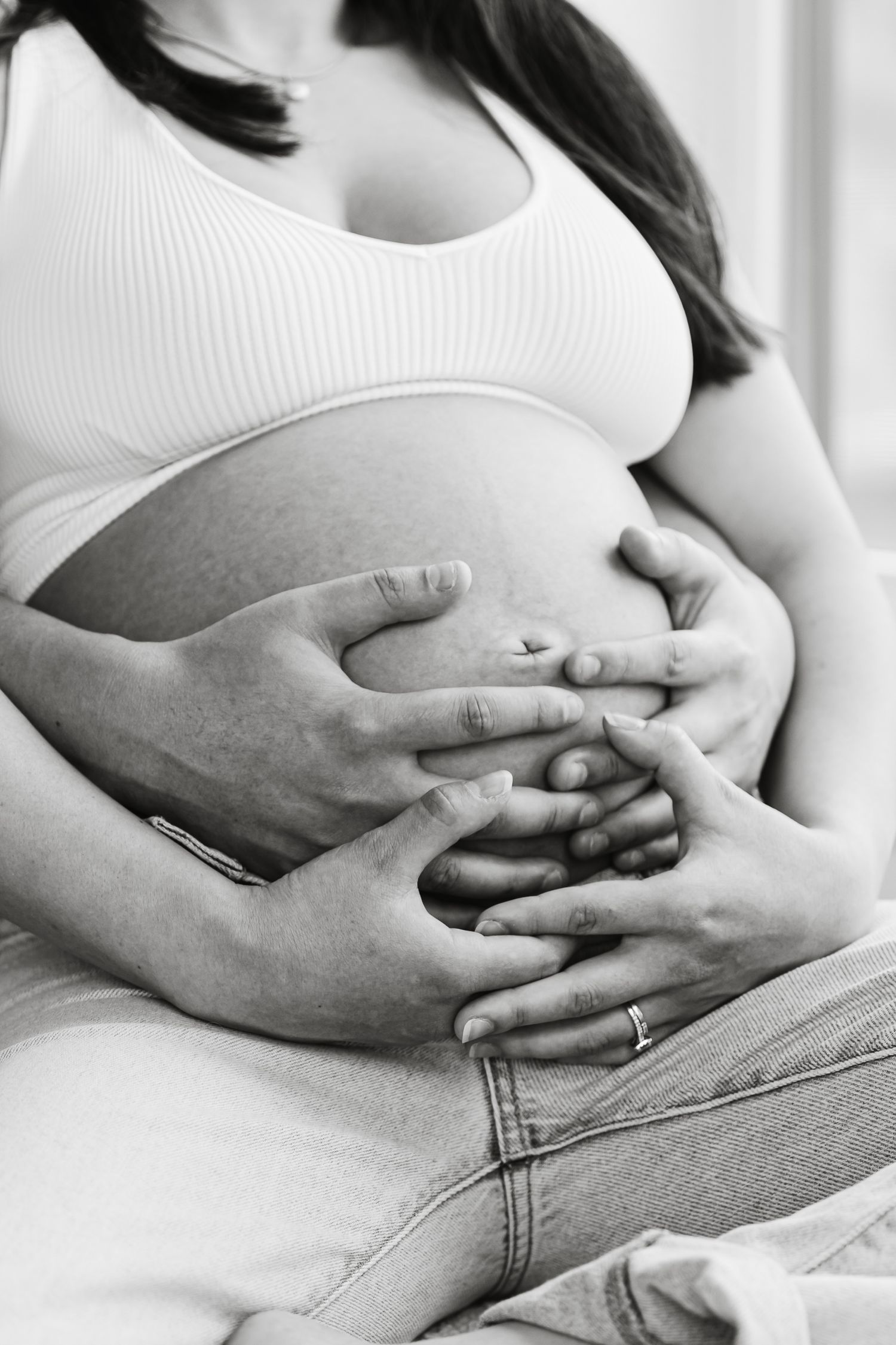 Black and white photo of pregnant woman with partner's hands cradling her bare baby bump.