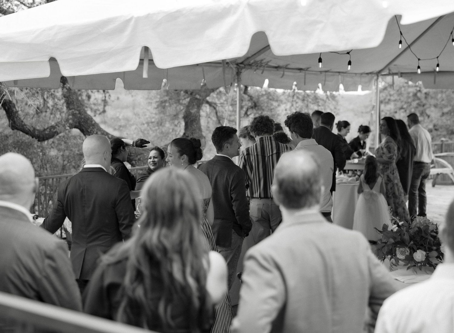 Wedding guests mingling under white tent at outdoor reception in black and white.