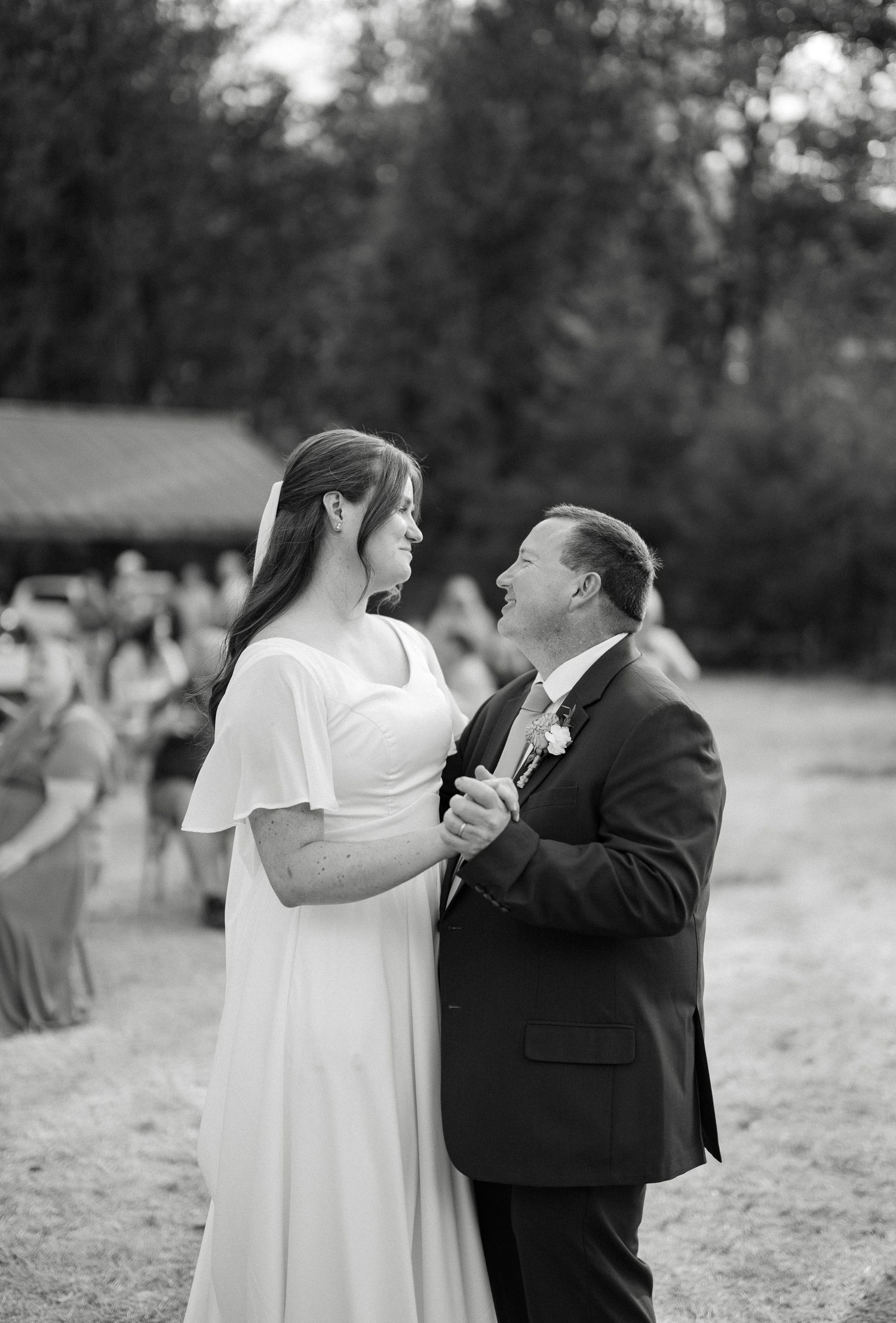Black and white photo of bride and father sharing an emotional first dance at outdoor wedding.