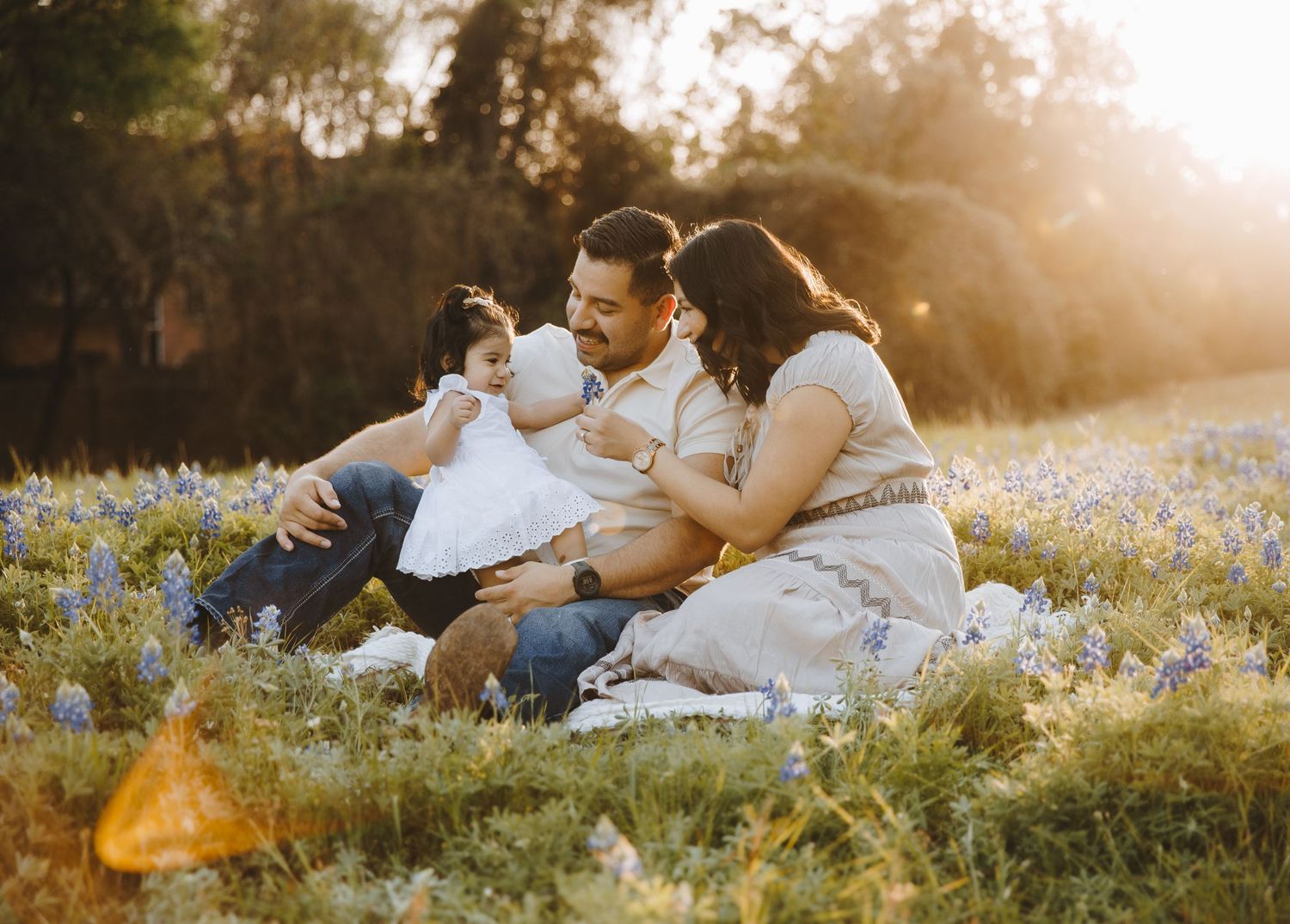 Young family sitting together in blooming bluebonnet field during golden hour sunset.