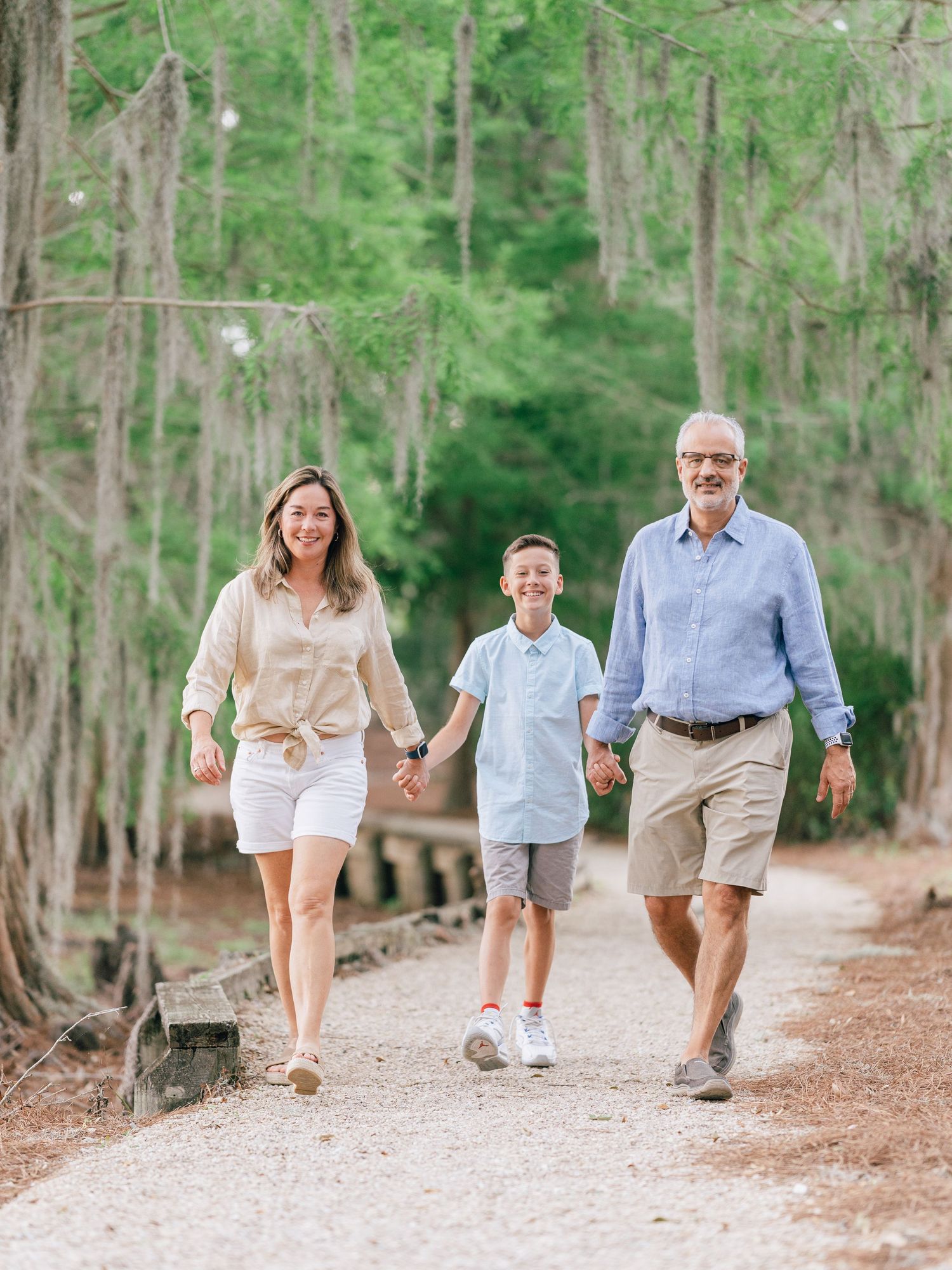 Family takes an afternoon stroll together on a nature trail surrounded by tall trees on a sunny day.