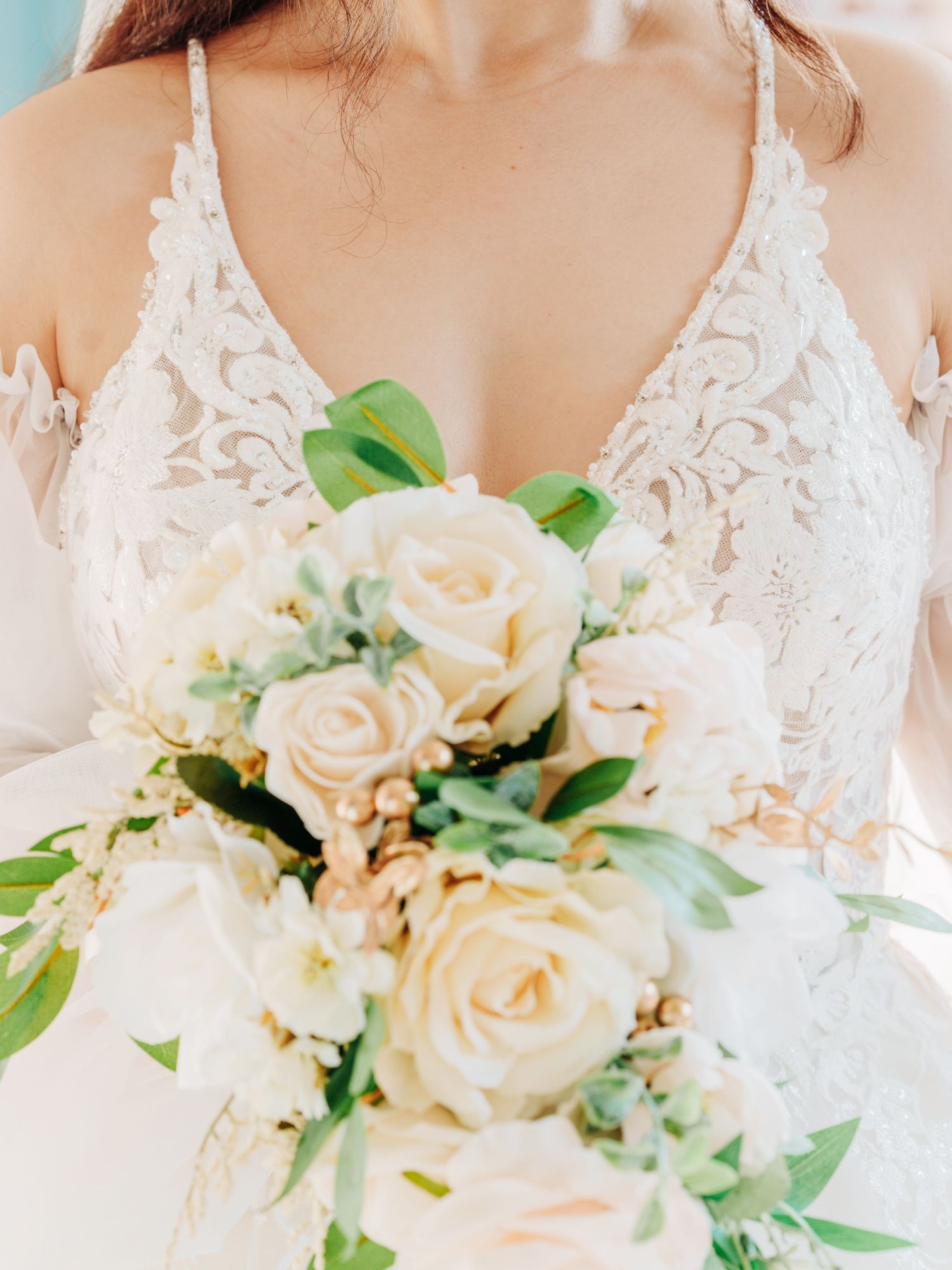A delicate white lace wedding dress bodice with a romantic cream rose and greenery bouquet.