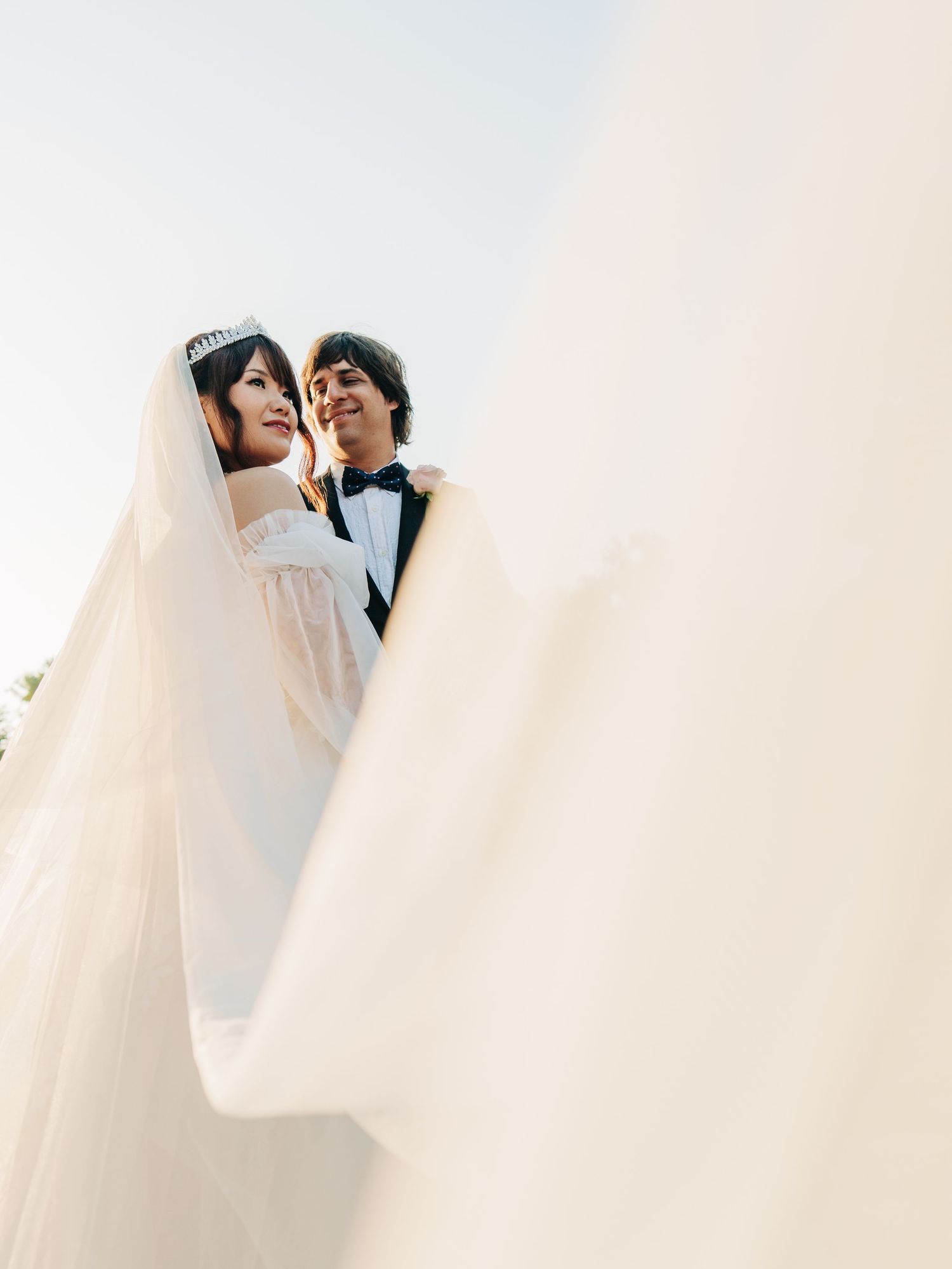 A tender wedding moment captured through flowing white veil fabric creating an artistic, romantic composition.